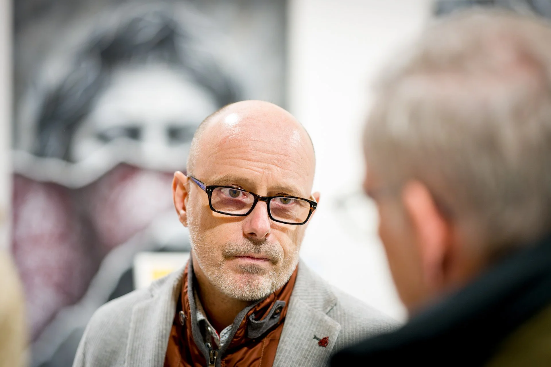 Brieuc Simon, portant des lunettes et une écharpe, écoute son interlocuteur lors du finissage de l’exposition de Noir Artist.