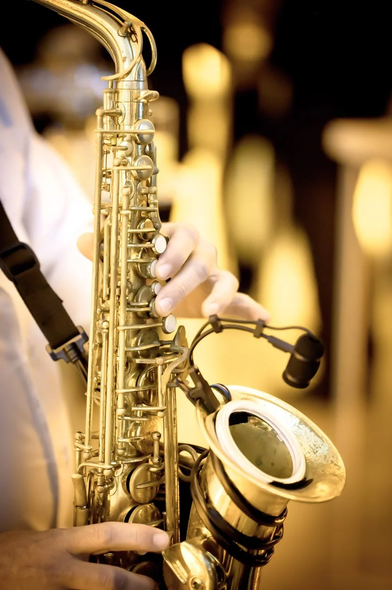 Saxophone en or avec un musicien qui joue, fond flou avec des chaises à l'arrière-plan.