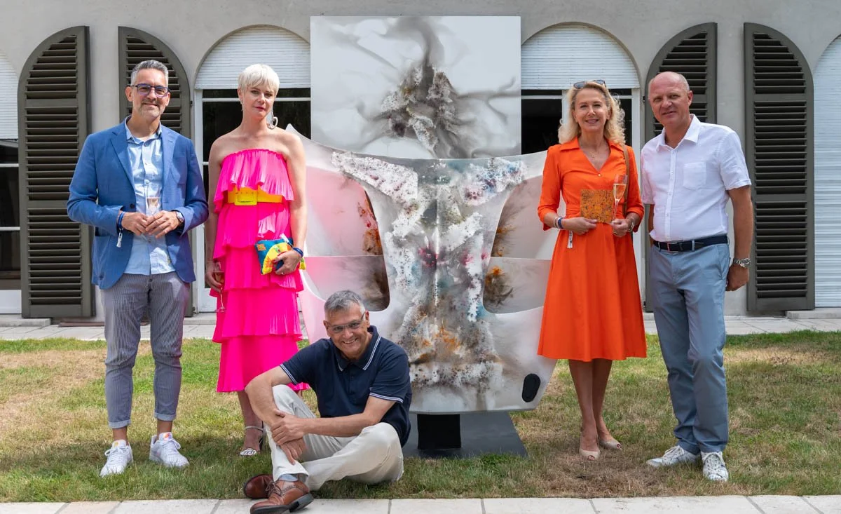 Cinq personnes posant autour d'une sculpture moderne à l'extérieur, avec un bâtiment en arrière-plan.