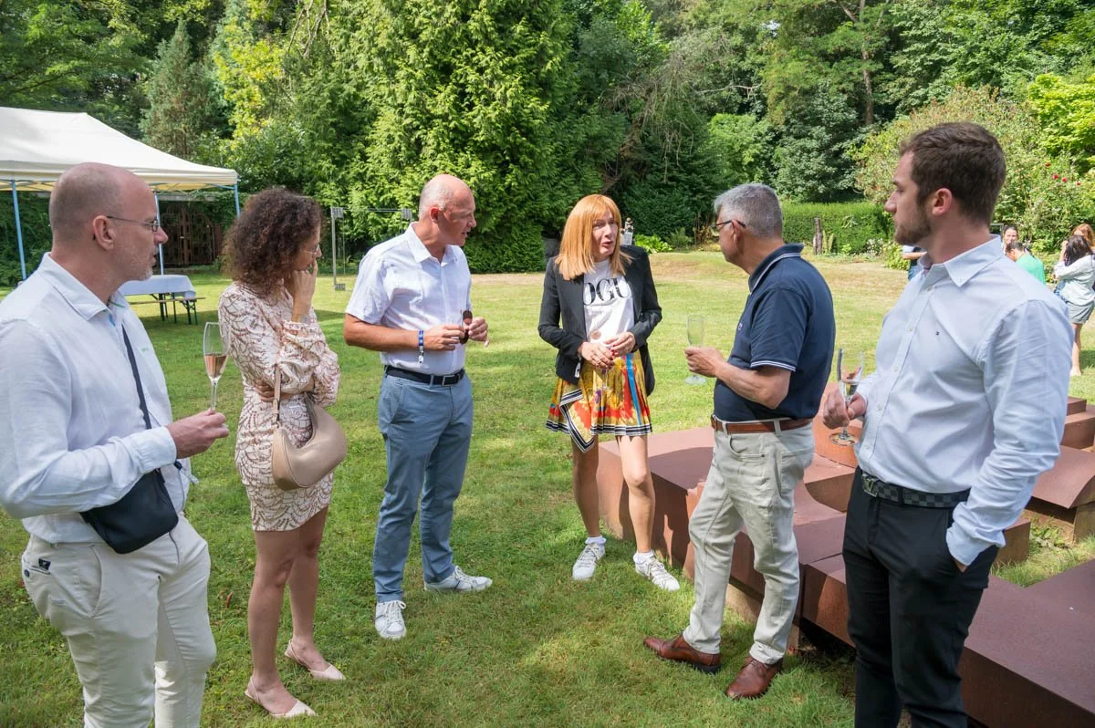 Groupe de personnes discutant dans un jardin lors d'un événement en plein air, avec verres à la main.