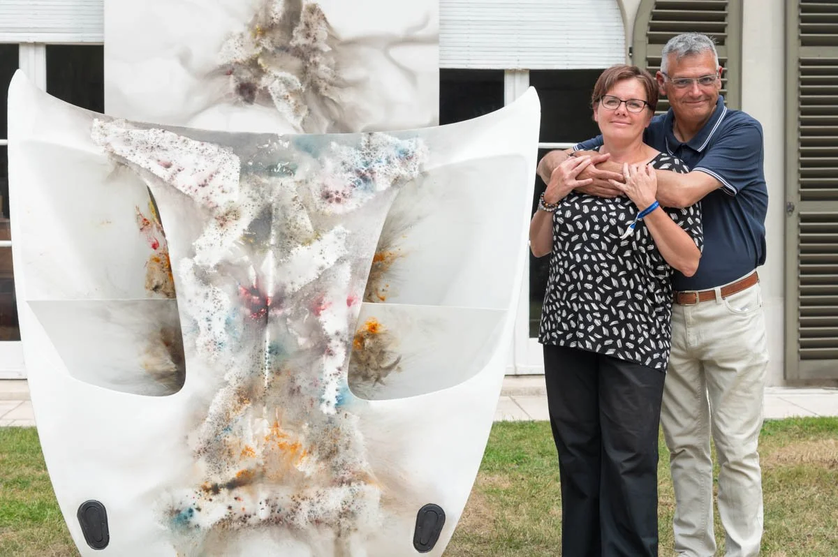 Un couple posé à côté d'une sculpture abstraite colorée en extérieur.
