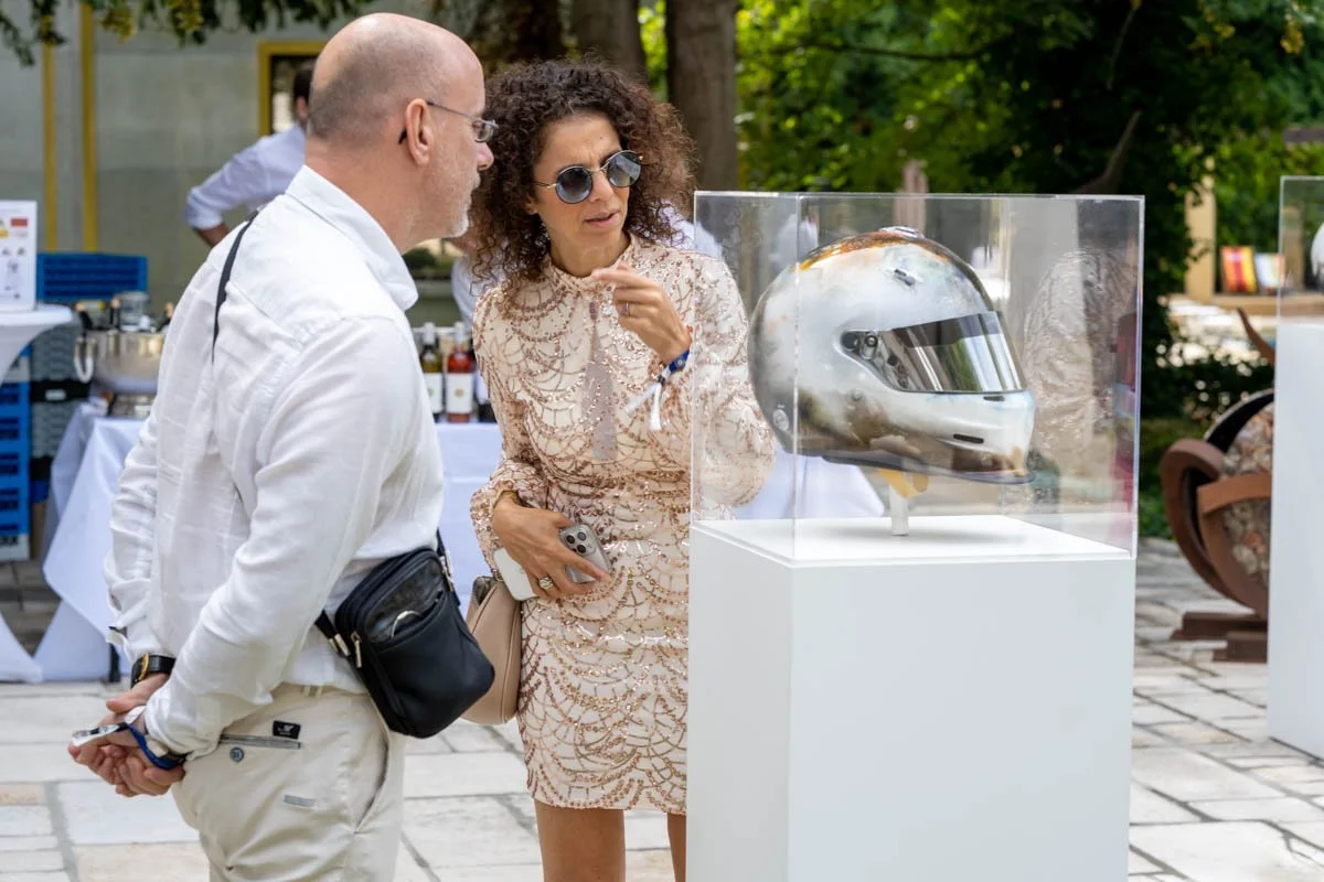 Deux personnes regardant un casque de course exposé dans une boîte vitrée.