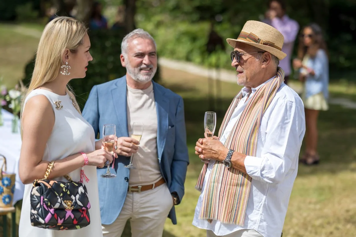 Trois personnes discutent lors d'un événement extérieur, tenant des flûtes de champagne.