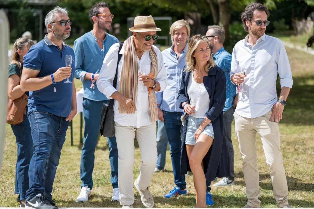 Groupe de personnes en plein air, en tenue décontractée, avec des verres à la main, lors d'un événement social.