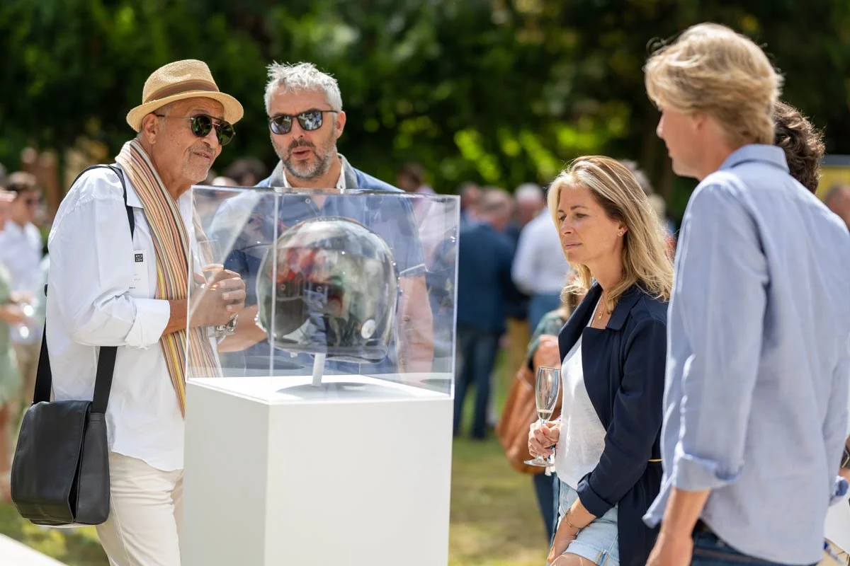 Des personnes regardent un casque exposé dans une vitrine transparente lors d'un événement en plein air.
