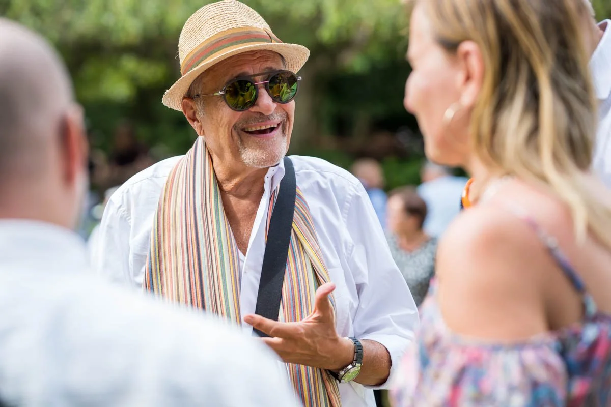 Un homme portant un chapeau et des lunettes de soleil parle à une femme, en plein air lors d'un événement social.