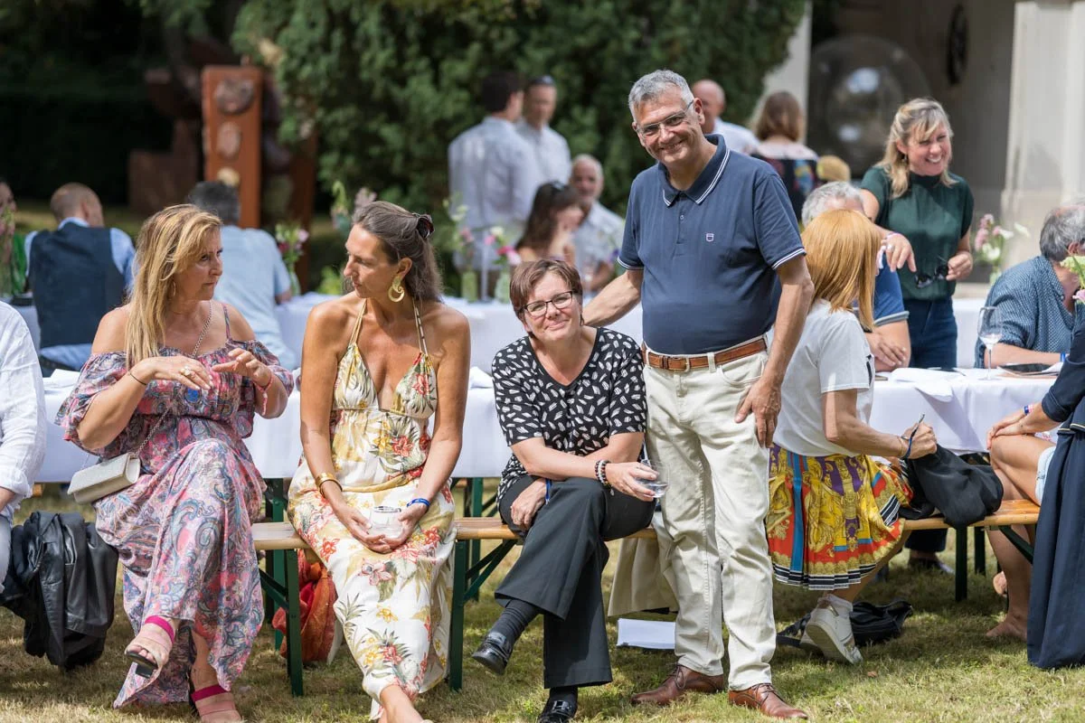 Groupe de personnes assises à l'extérieur lors d'un événement social, discutant et souriant.