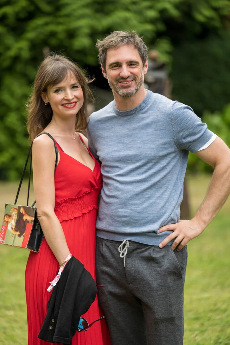 Un homme et une femme posant ensemble dans un jardin, la femme en robe rouge et l'homme en t-shirt bleu.