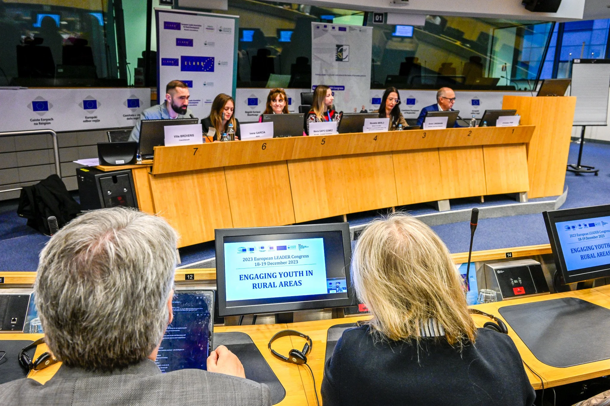 Conférence avec un panel de personnes assises à une table, écrans montrant "Engaging Youth in Rural Areas", Congrès Leader Européen 2023, Bruxelles. Participants regardent la présentation.