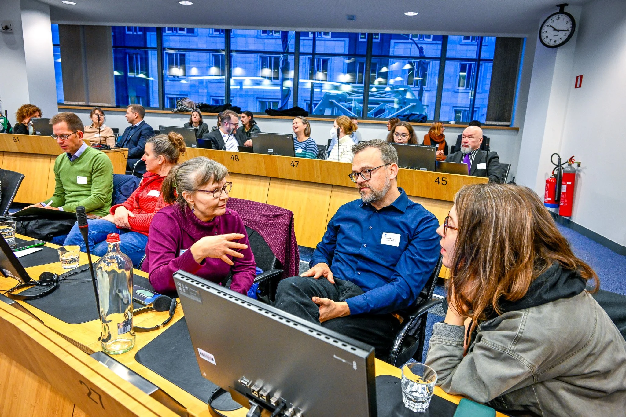 Groupe de personnes discutant dans une salle de réunion avec ordinateurs et bouteilles d'eau.