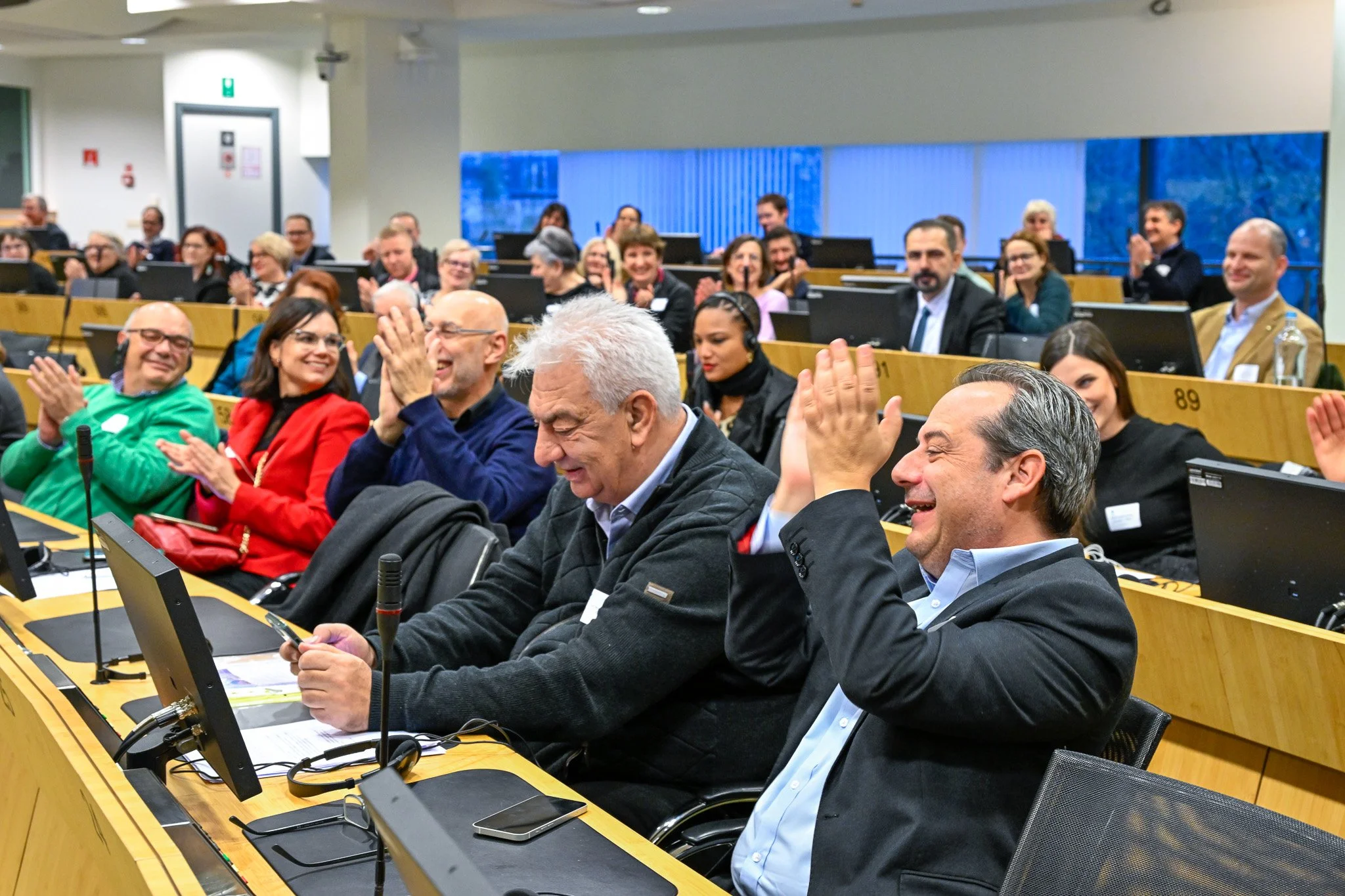 Un groupe de personnes dans une salle de conférence applaudissant avec des ordinateurs portables sur les tables.