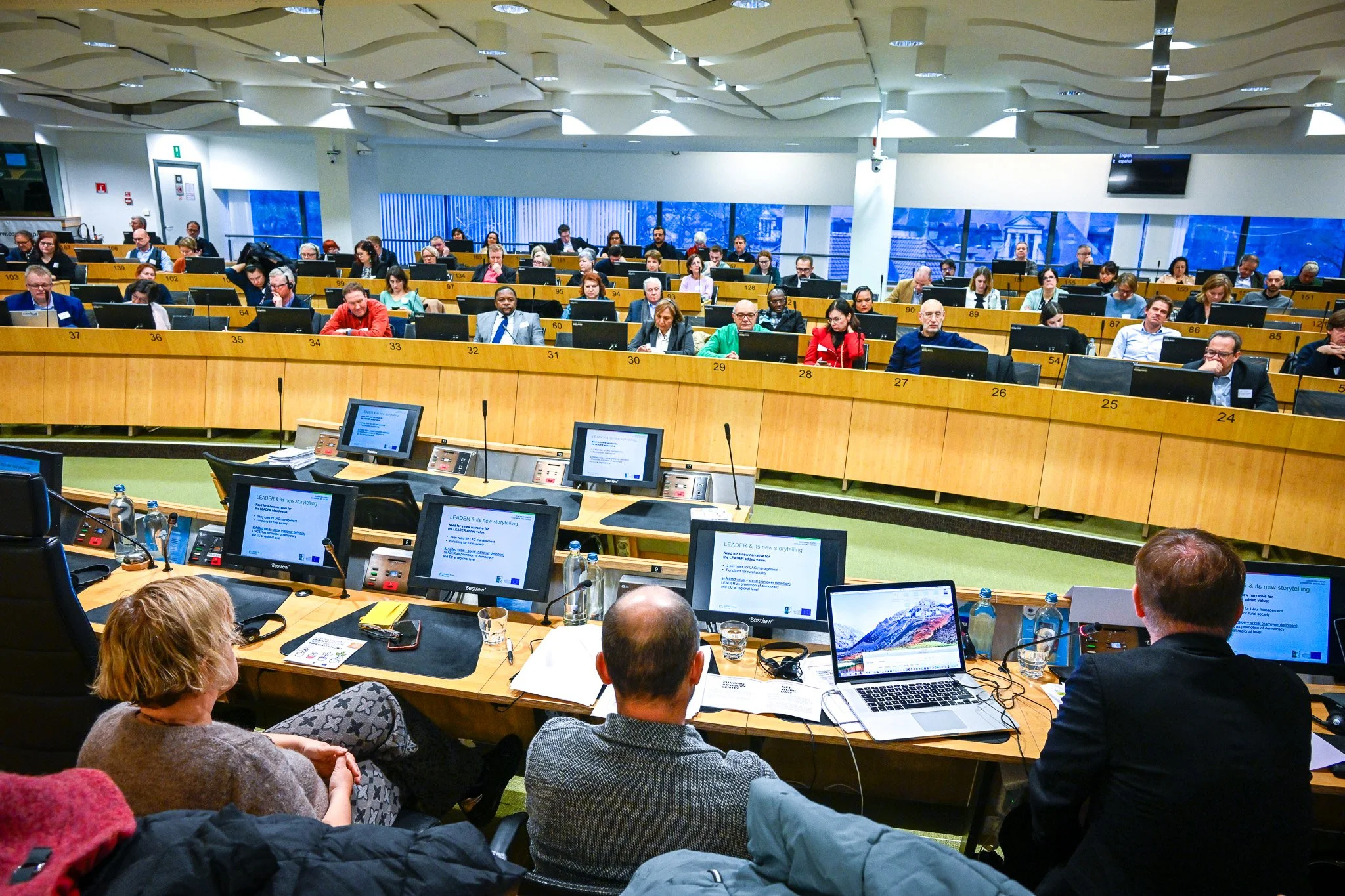 Salle de conférence avec des participants assis devant des écrans et des microphones, vue depuis la table de présentation