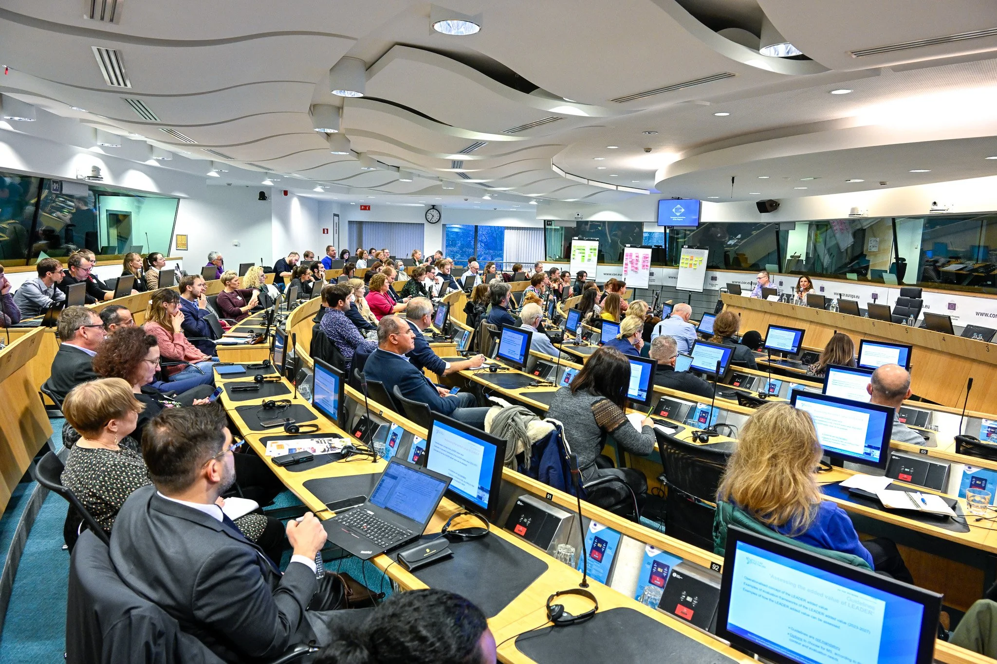 Salle de conférence avec de nombreuses personnes assises devant des ordinateurs portables, écoutant une présentation.