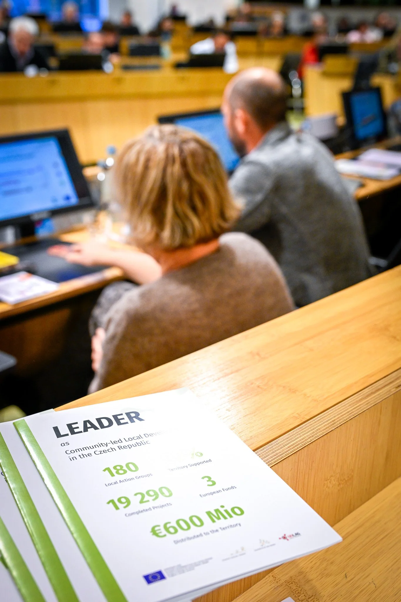 Des personnes assises devant des ordinateurs dans une salle de réunion, avec un document en premier plan intitulé "LEADER" concernant le développement local en République Tchèque.