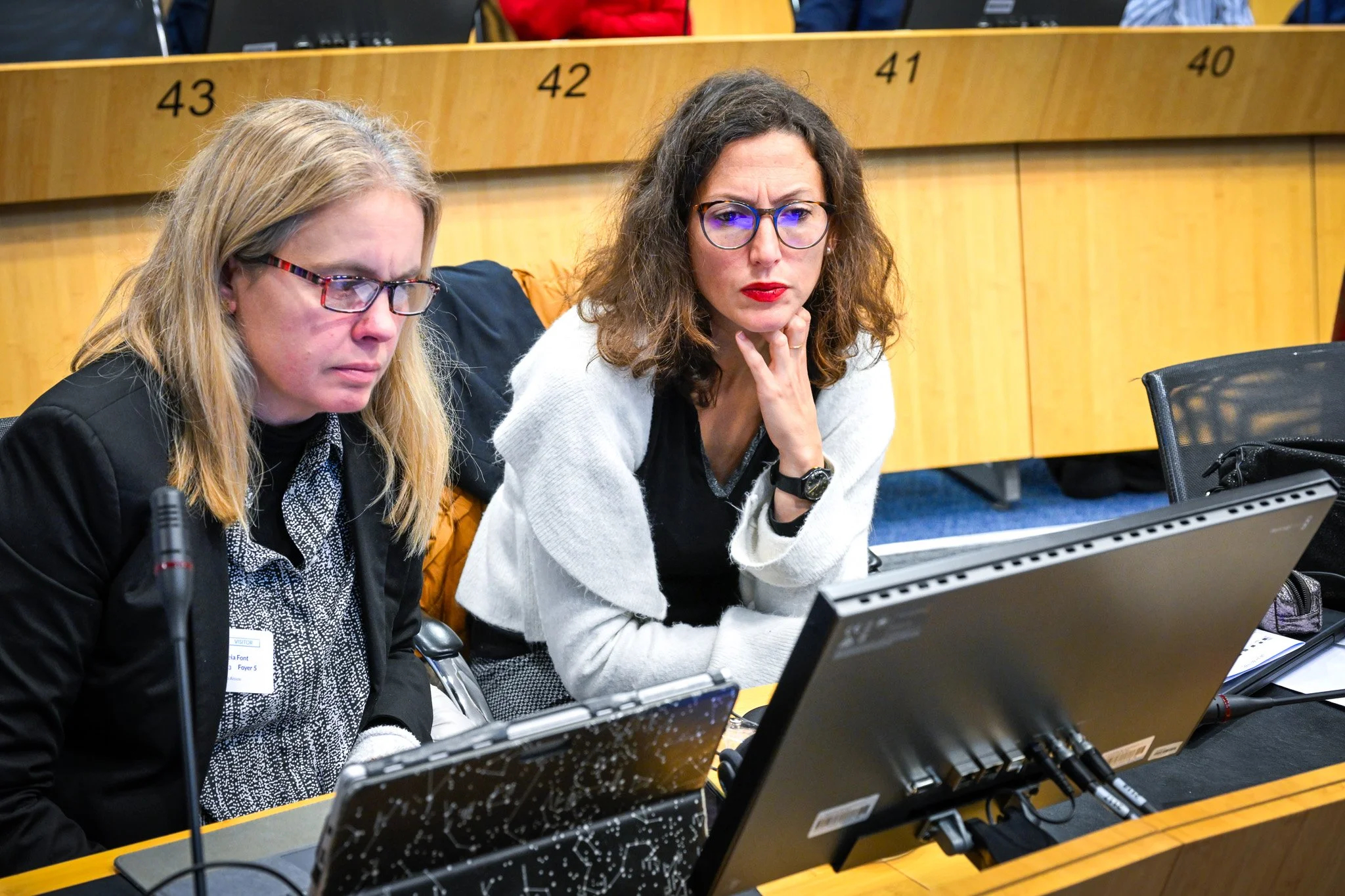 Deux femmes concentrées regardent un écran d'ordinateur lors d'une réunion ou conférence.