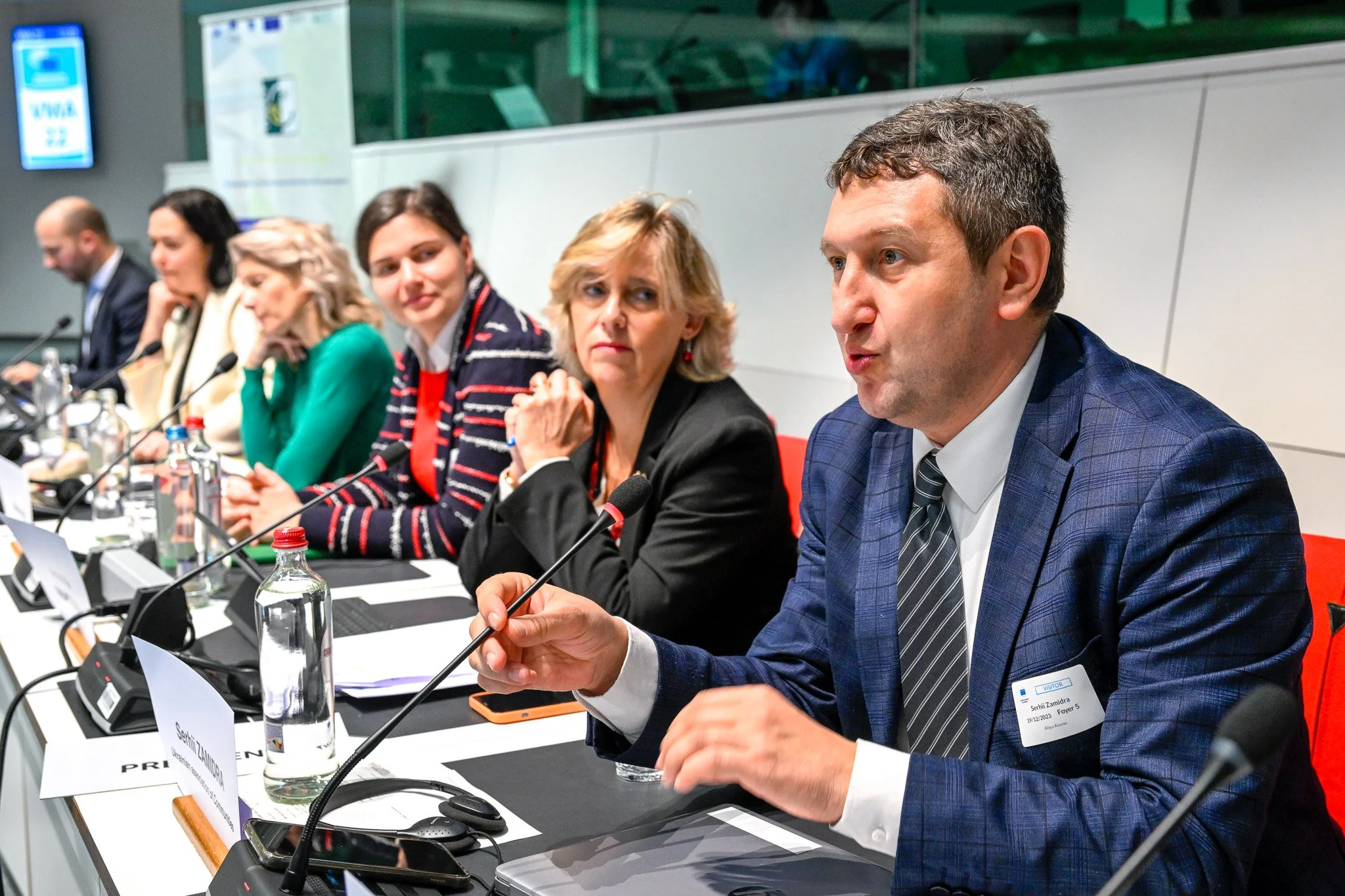Personnes assises à une table de conférence, prenant la parole avec des micros, dans un cadre professionnel.