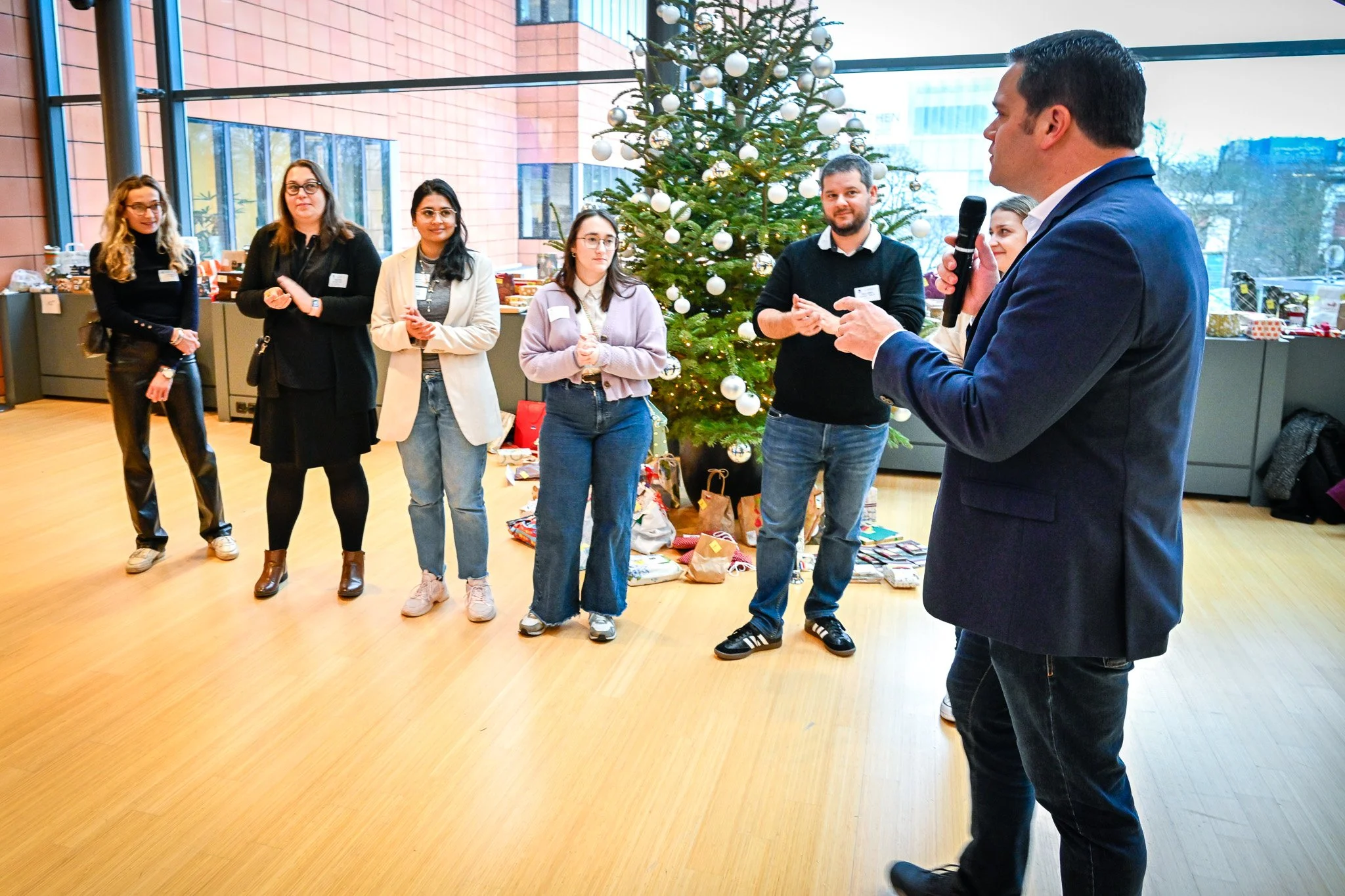 Photo d'un événement organisé dans les locaux du Comité des Régions à Bruxelles. Groupe de personnes debout à l'intérieur, près d'un sapin de Noël décoré, un homme tenant un microphone.