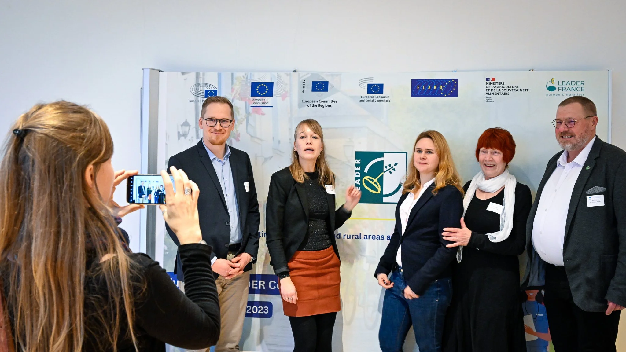 Un groupe de personnes posant pour une photo lors d'un événement européen, avec des logos institutionnels en arrière-plan.