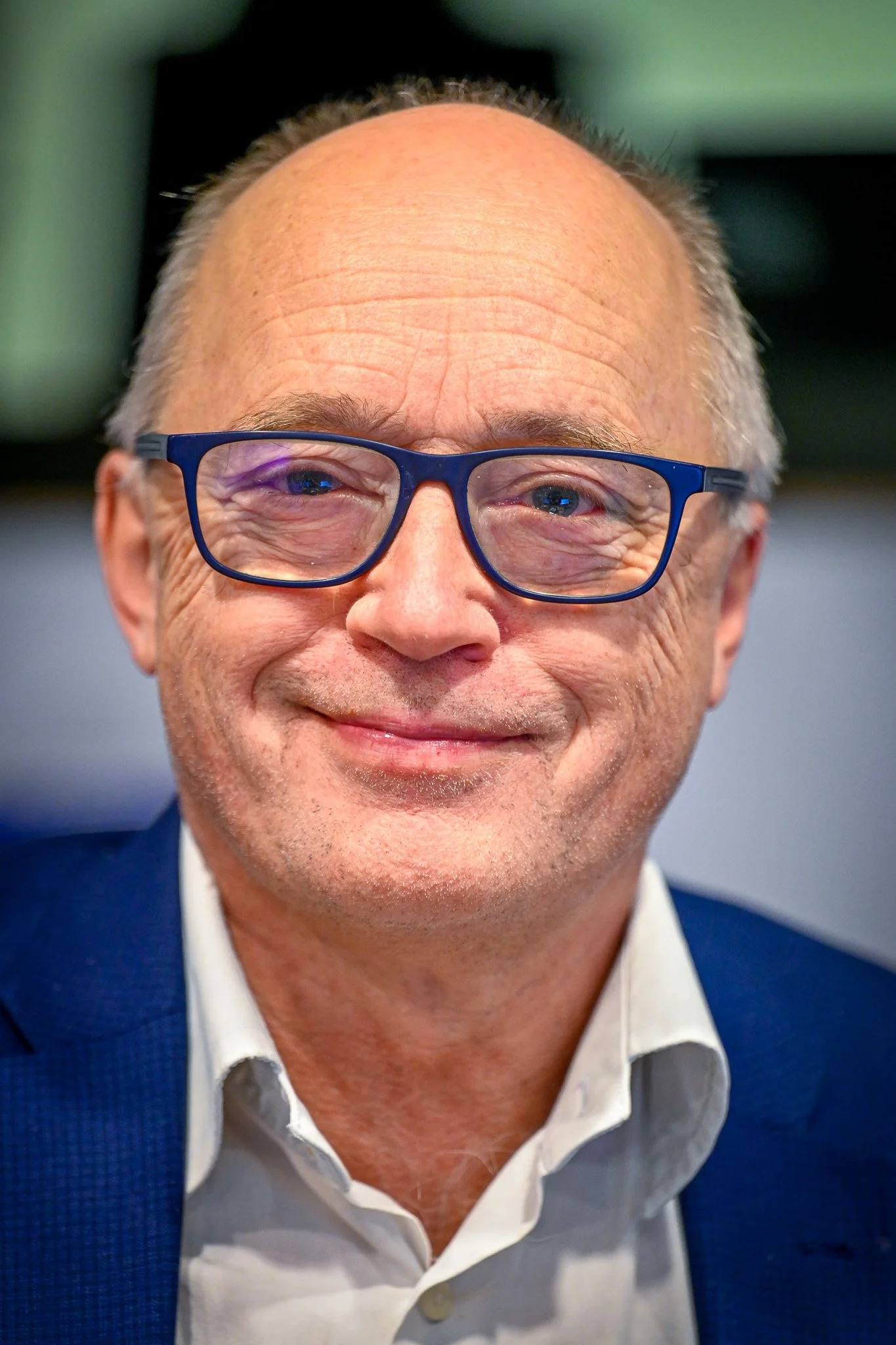 Homme souriant portant des lunettes et un costume bleu.