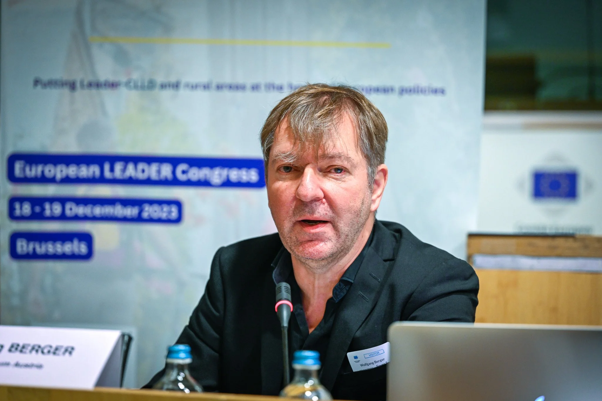 Un homme s'exprime lors du Congrès LEADER européen à Bruxelles, les 18-19 décembre 2023. Il est assis devant un micro, avec un badge portant le nom Wolfgang Berger. En arrière-plan, une affiche avec le nom de l'événement."