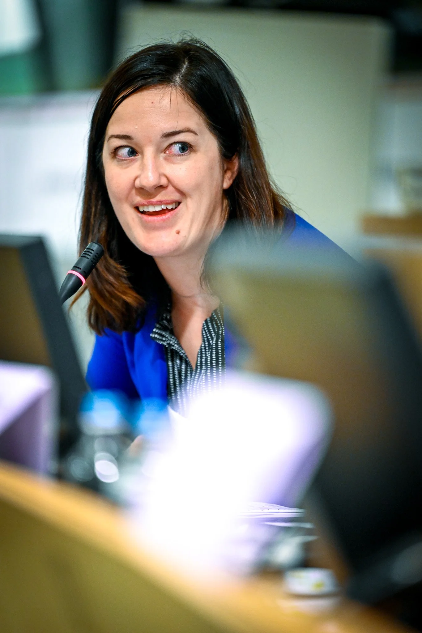 Femme souriante avec micro en réunion, portant une veste bleue.