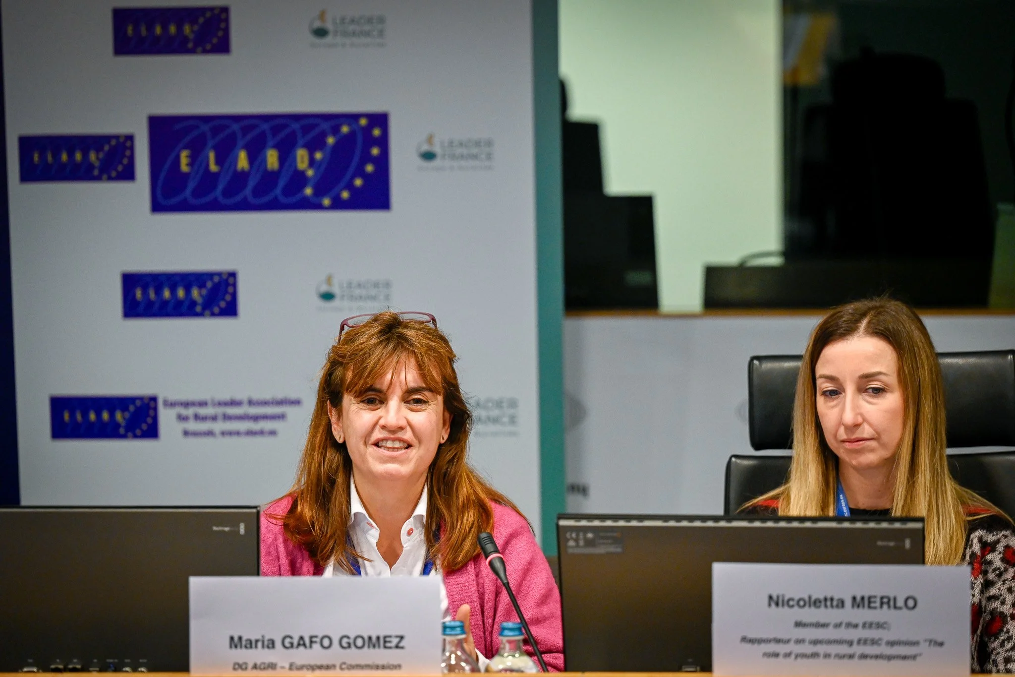 Deux femmes assises devant des ordinateurs lors d'une conférence, avec des panneaux affichant "ELARD" en arrière-plan.