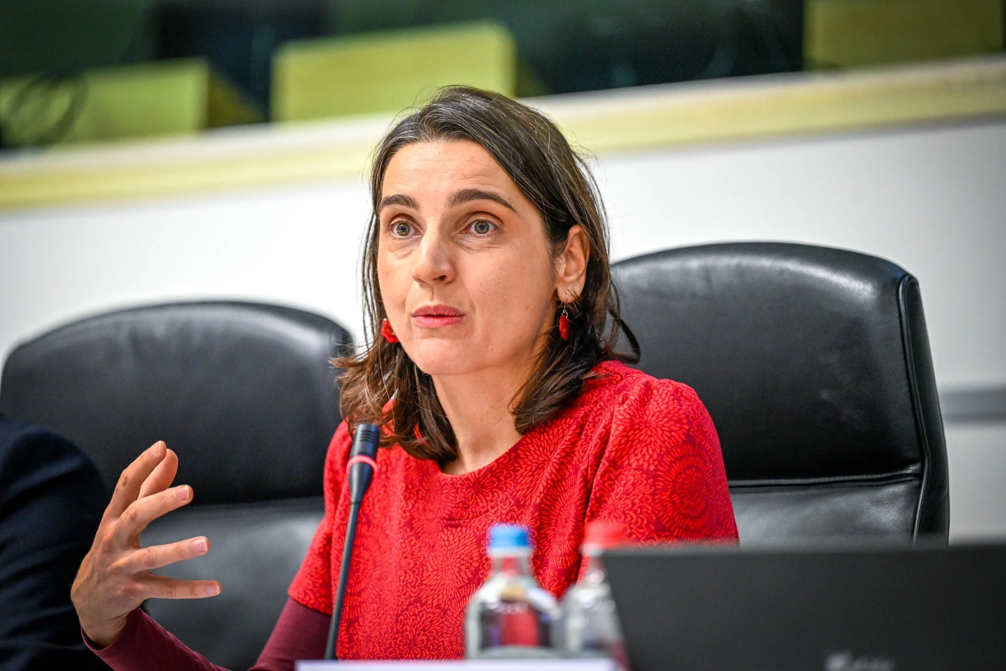 Une femme en rouge parle dans un micro lors d'une conférence.