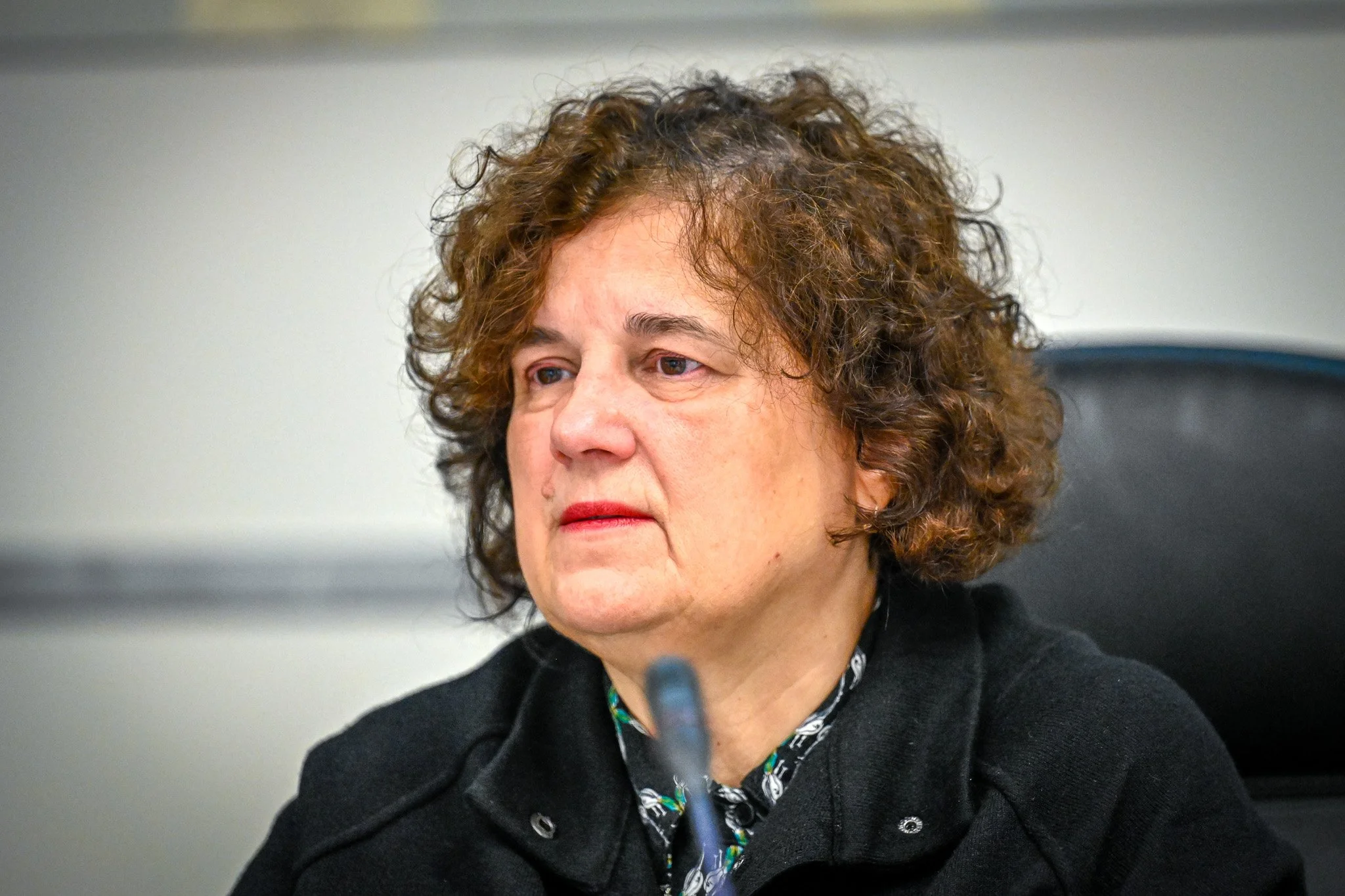 Femme assise avec des cheveux bouclés et portant un manteau noir.
