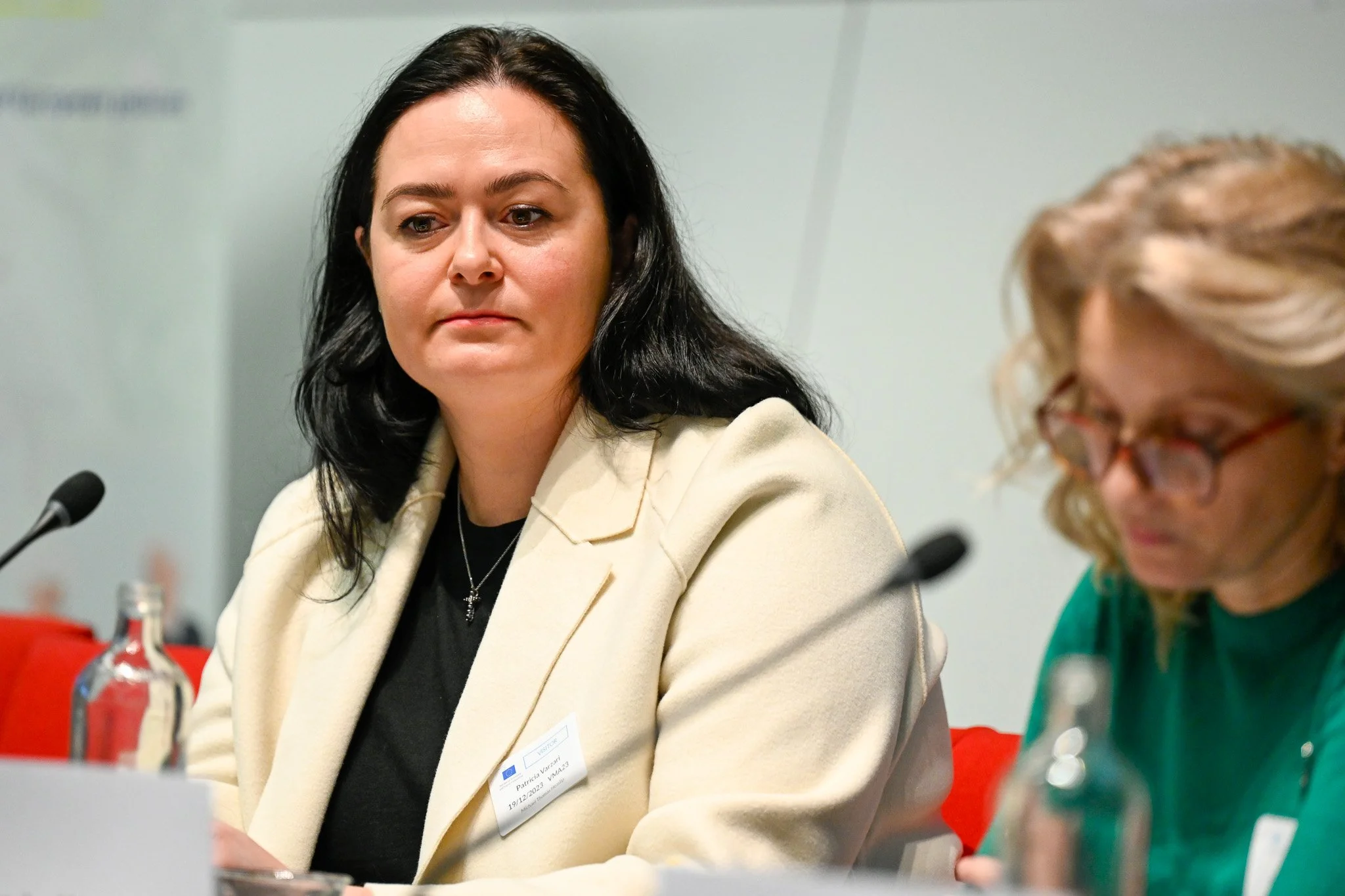 Deux femmes à une conférence, l'une en veste crème et l'autre écrivant.