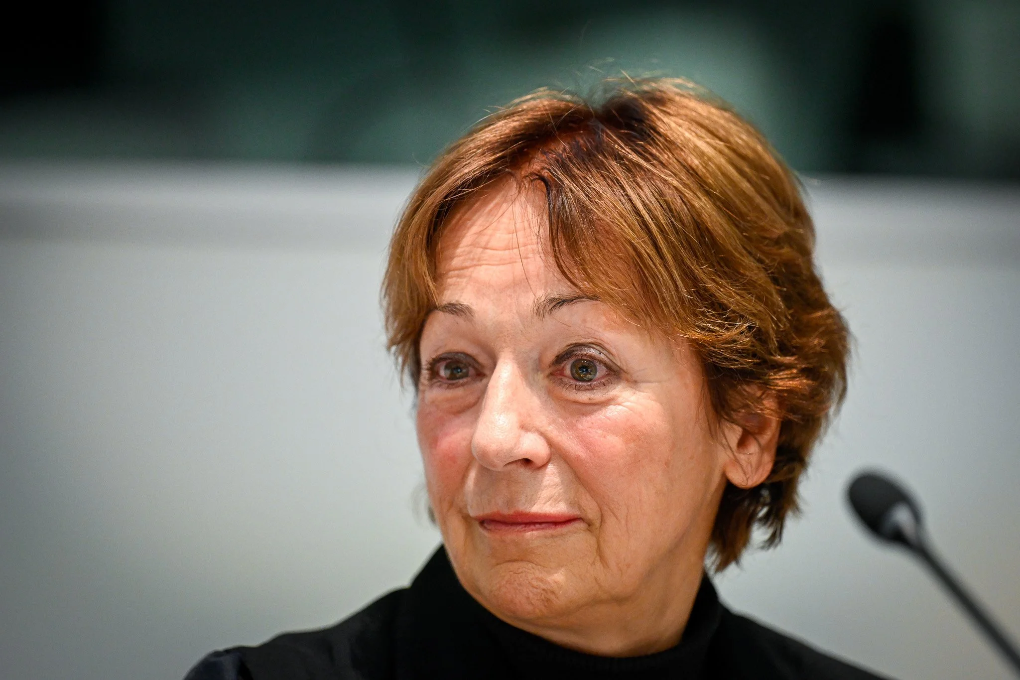 Femme âgée avec des cheveux courts brun clair, assise devant un microphone.