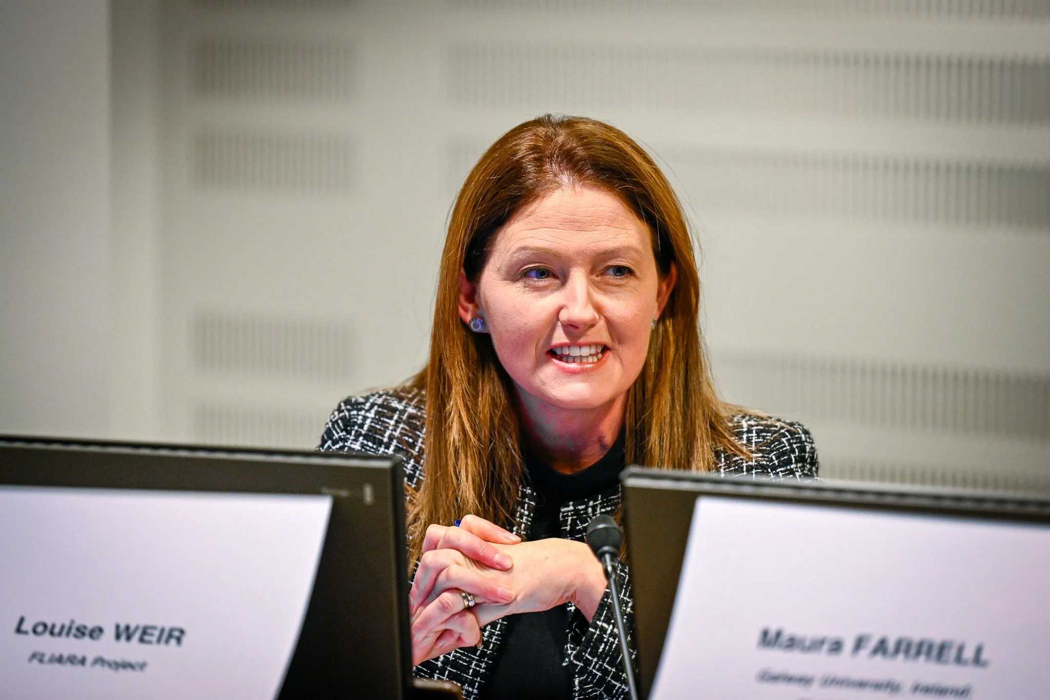 Femme parlant à un podium avec deux écrans visibles.