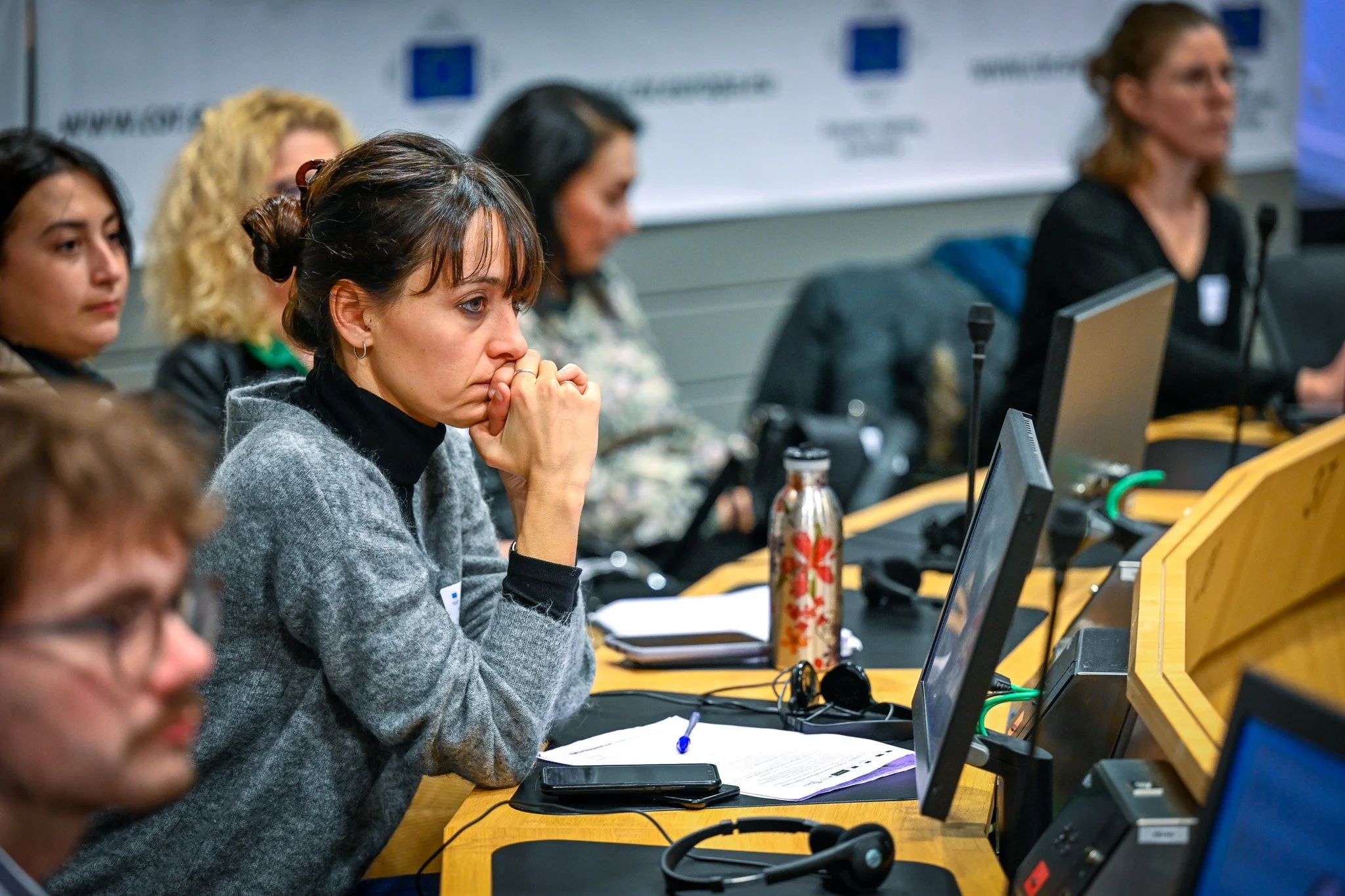 Des personnes assises à une table lors d'une conférence, avec des écrans d'ordinateur et des écouteurs.