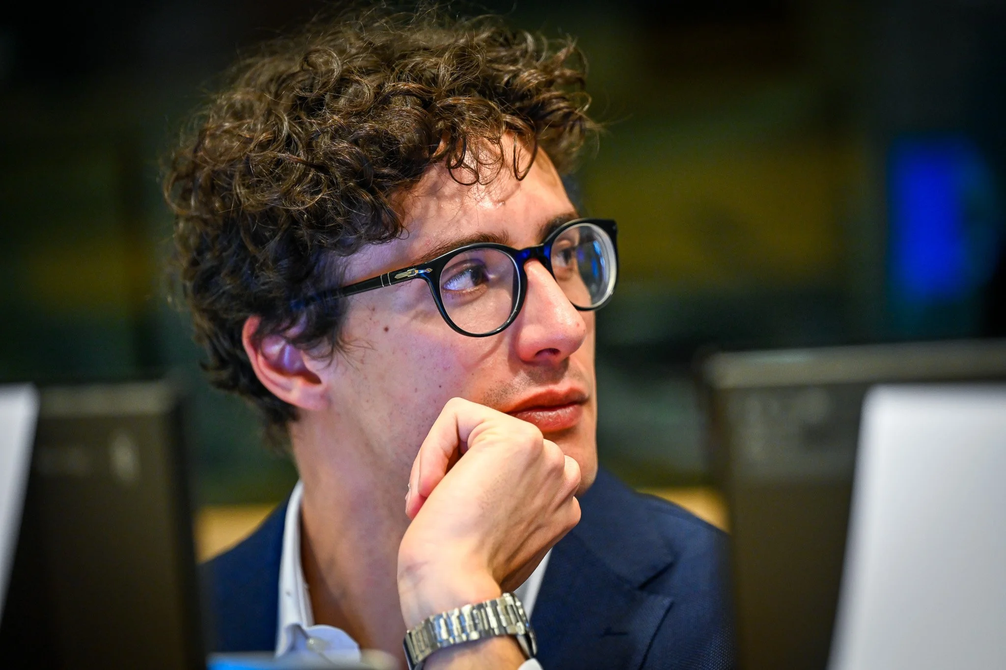 Homme portant des lunettes regardant sur le côté avec sa main sur le menton.