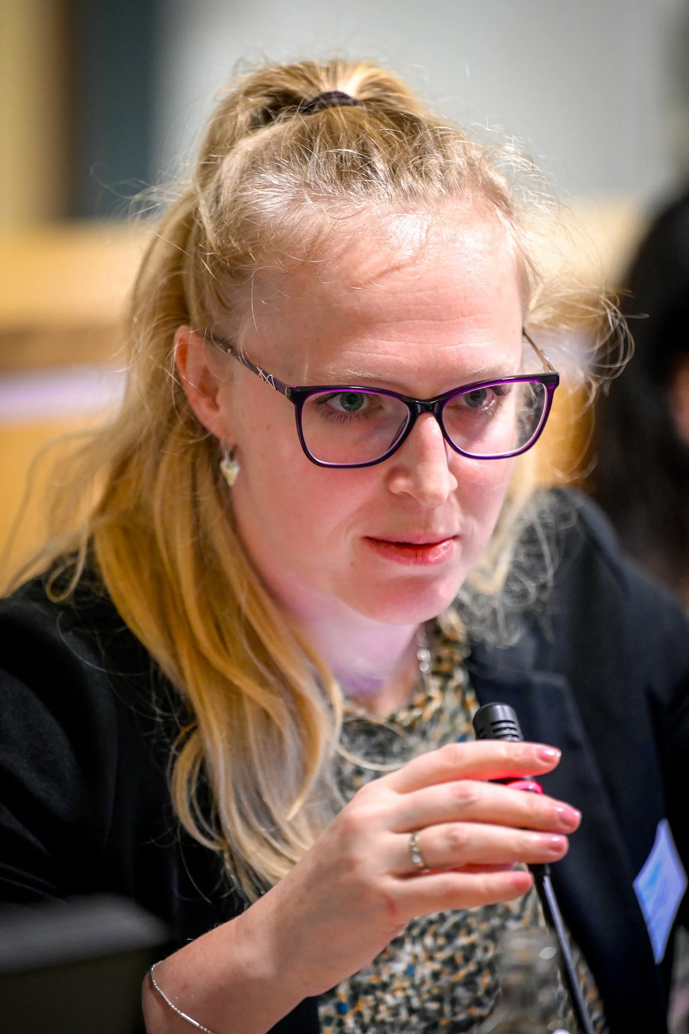 Une femme avec des lunettes parlant dans un micro lors d'une réunion.