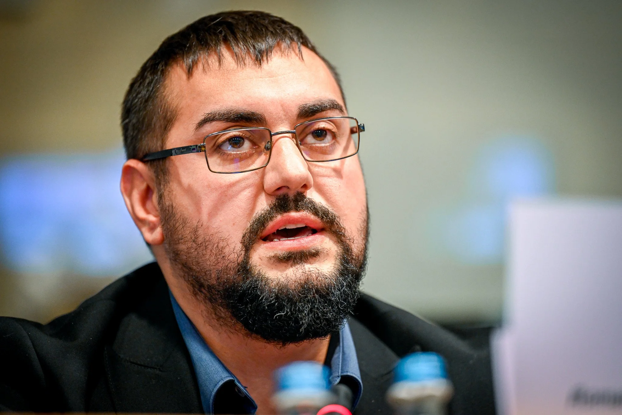 Un homme avec des lunettes et une barbe parle, probablement lors d'une conférence ou réunion.