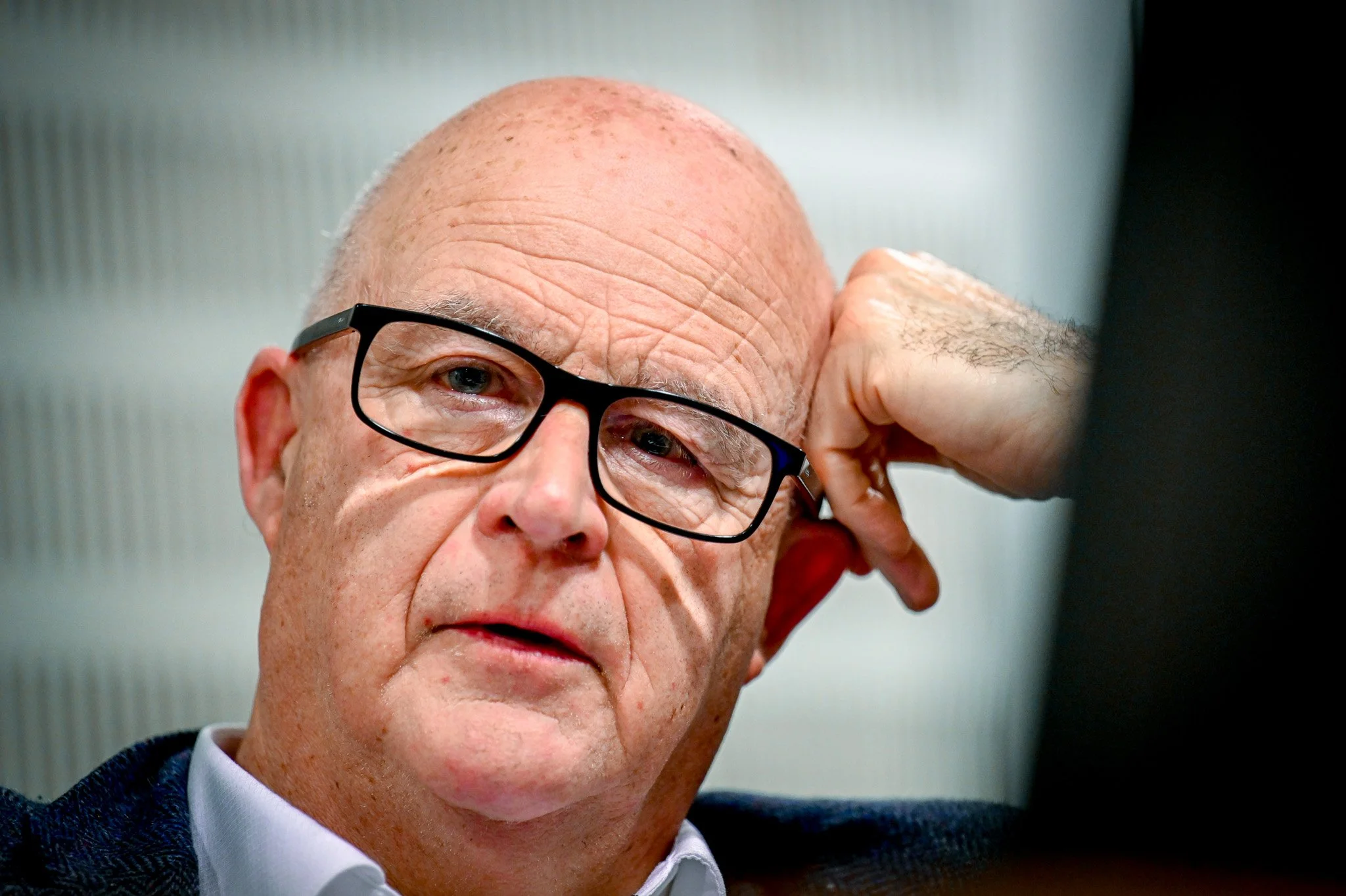 Homme portant des lunettes, posant sa tête sur sa main, expression sérieuse.