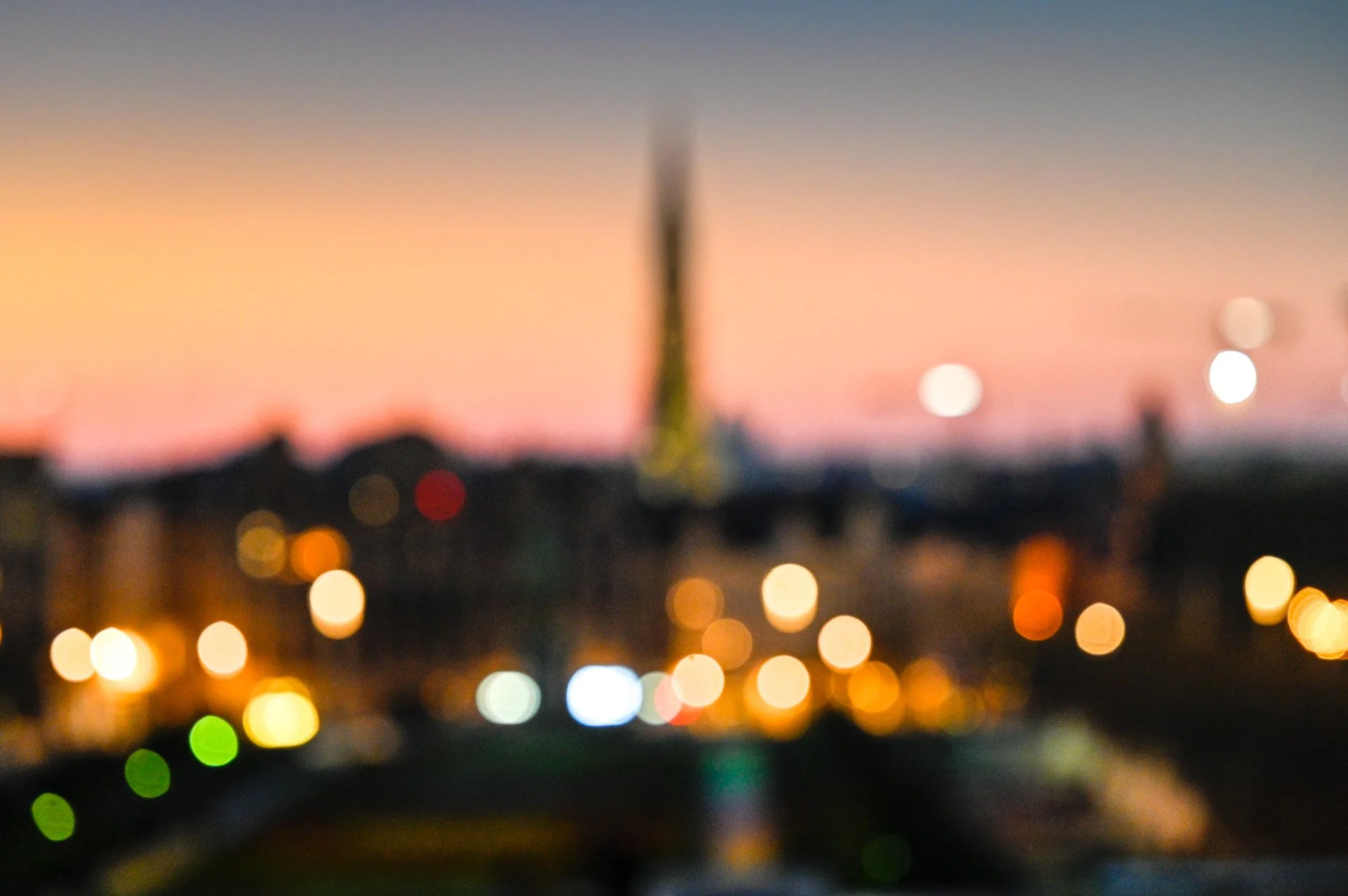 A deliberately blurred view of Brussels at sunset, with a spire on the horizon and points of light in the foreground.