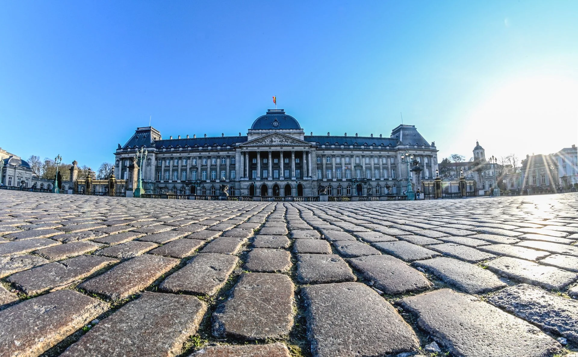 The Royal Palace in Brussels under a blue sky, photographed at cobblestone level on the Place des Palais.