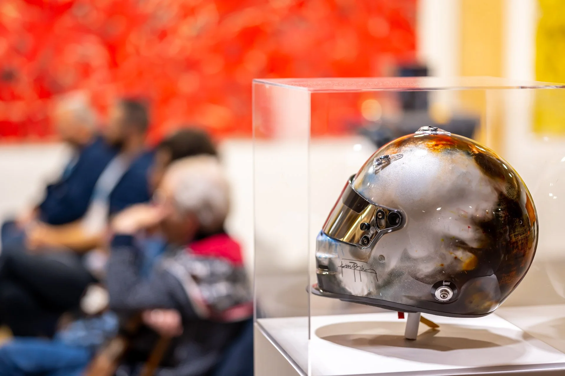 Casque de moto avec design artistique, exposé dans une vitrine, flou des visiteurs en arrière-plan.