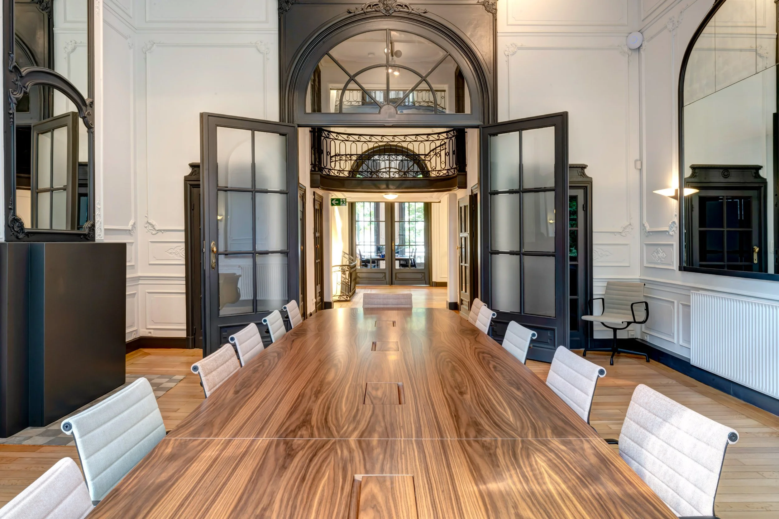 Salle de réunion avec une grande table en bois, chaises en tissus beige, miroirs et portes en verre dans un intérieur élégant. Font un espace lumineux avec fenêtres à l'arrière.
