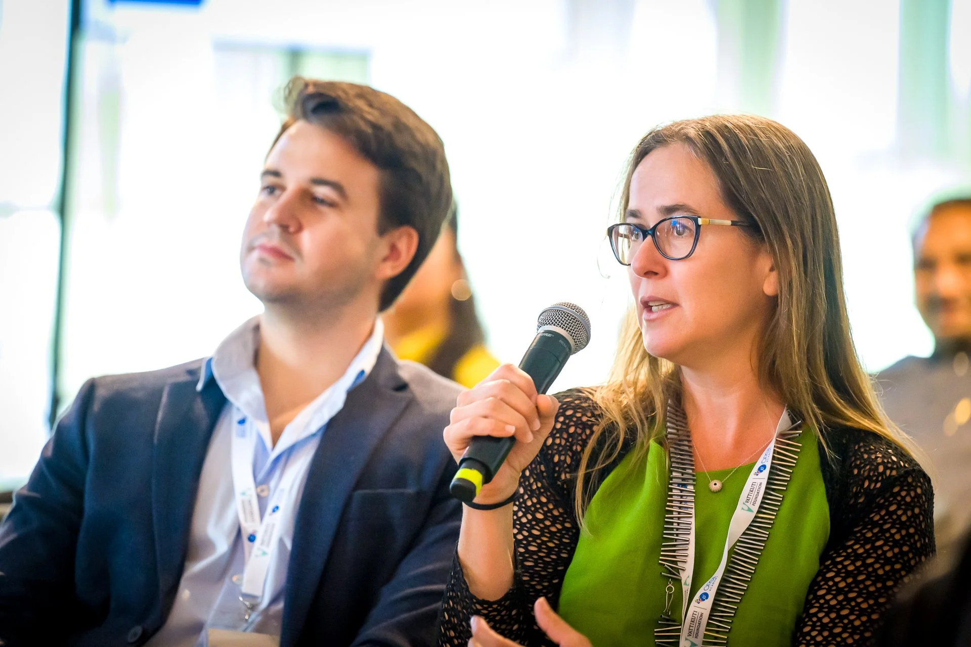 Deux personnes participent à une conférence, une femme tient un microphone pour poser une question ou faire un commentaire.