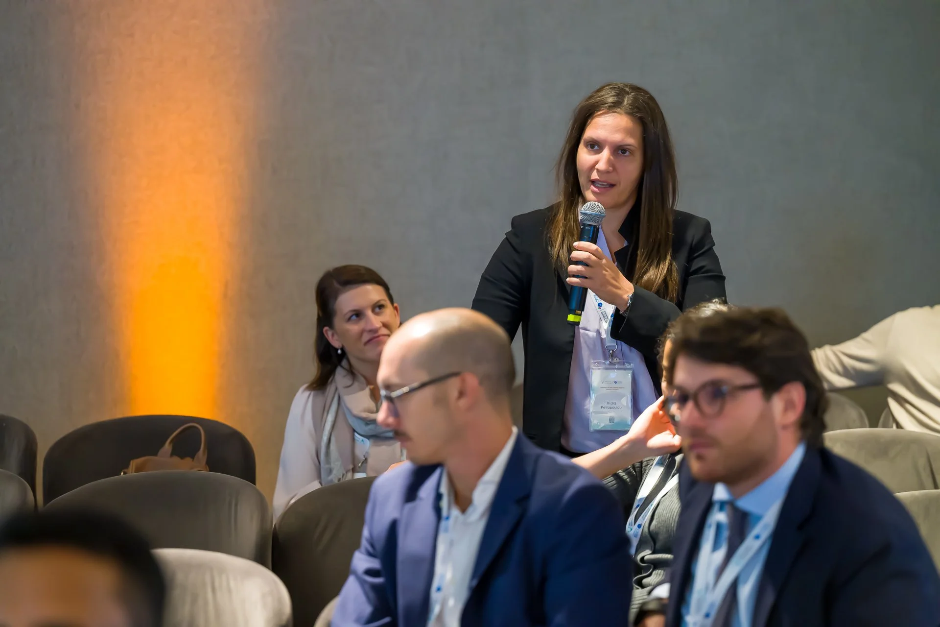 Une femme tenant un microphone parle lors d'une conférence, entourée de personnes assises.
