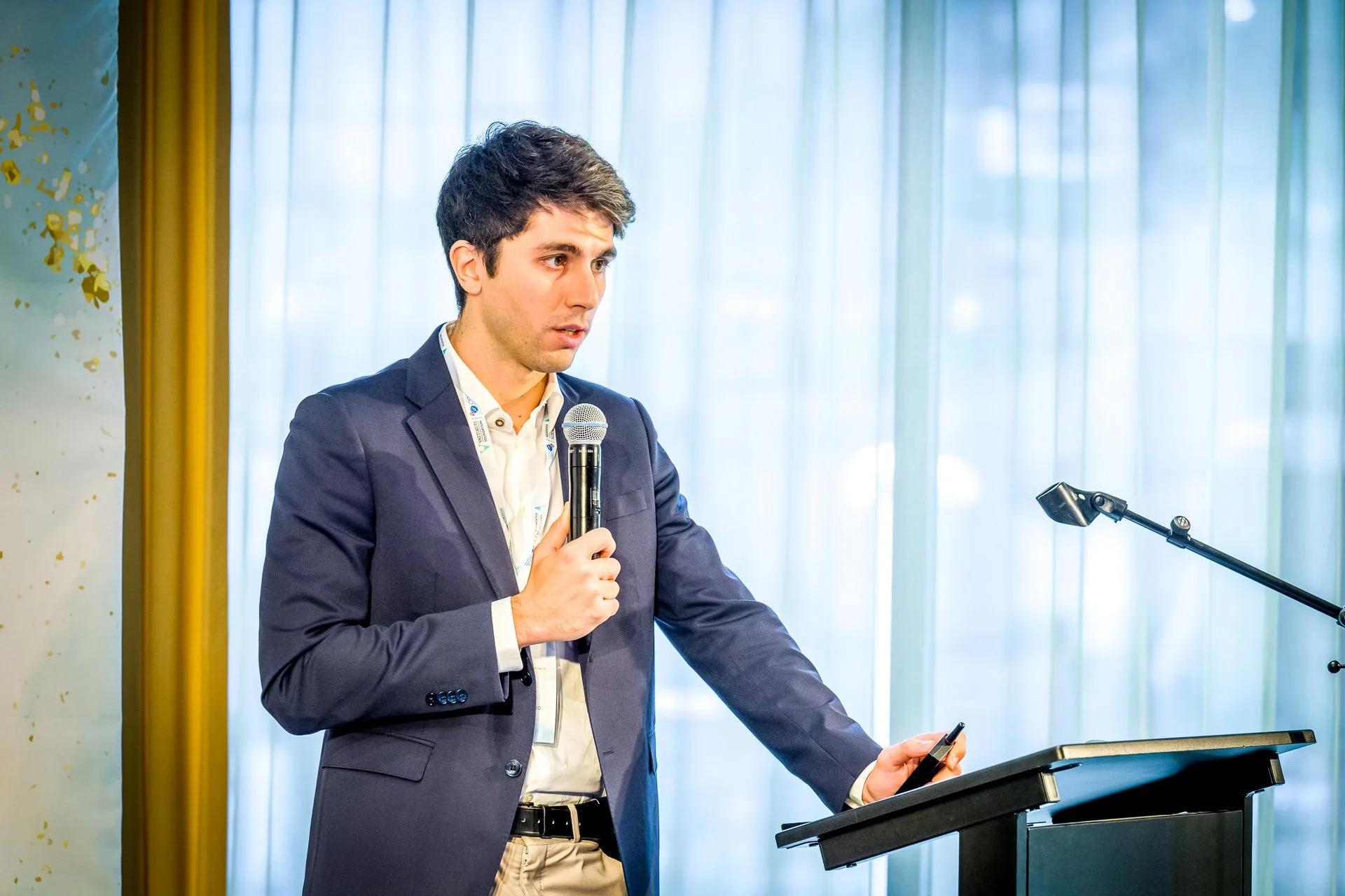 Un homme en costume parle dans un micro sur un podium lors d'une conférence.
