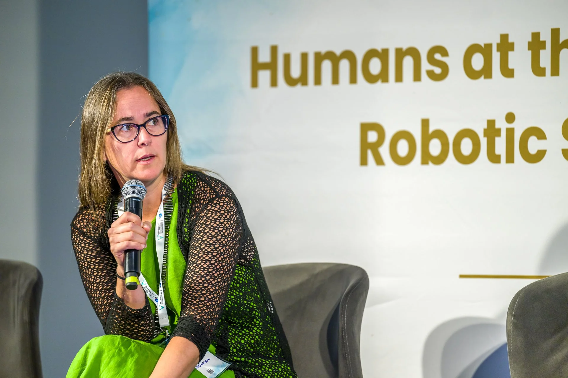 Photo pendant une conférence qui montre une femme tenant un micro lors d'une conférence avec une banderole en arrière-plan indiquant "Humans at the Robotic Summit".