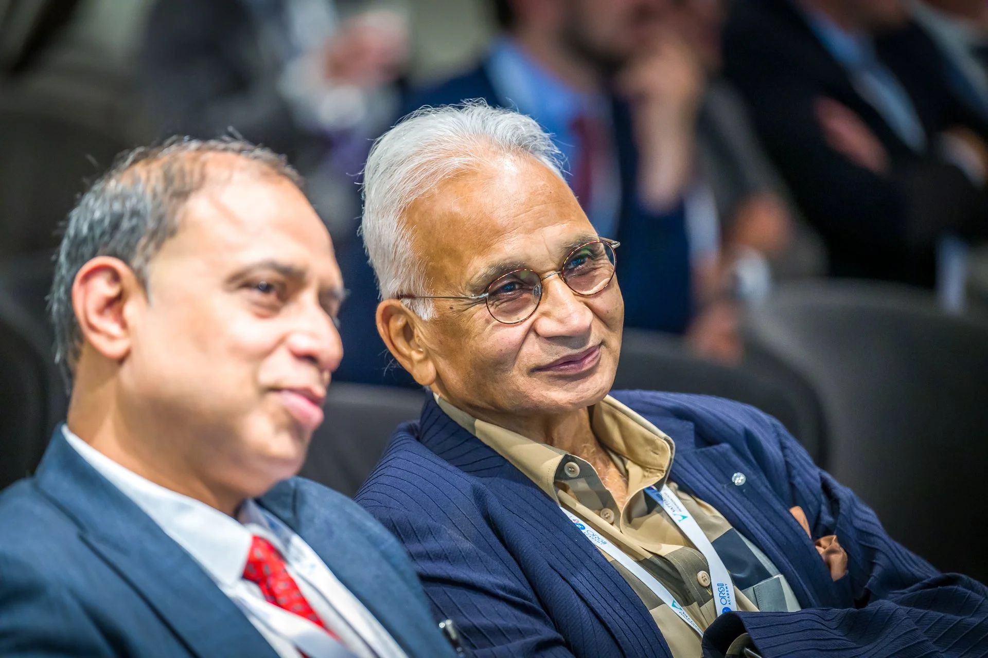 Deux hommes souriants assis côte à côte, habillés en tenue de ville, lors d'une conférence.
