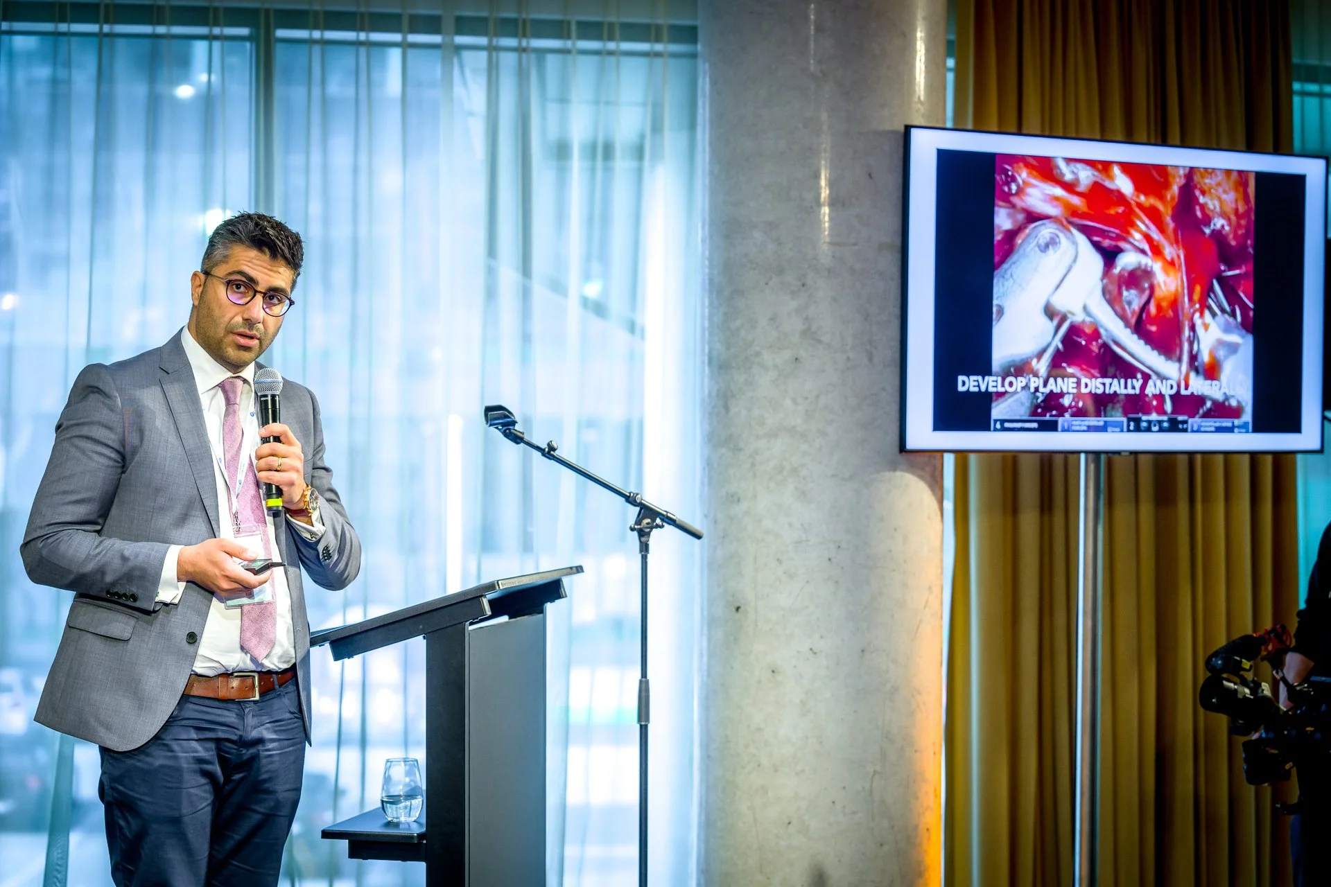 Homme en costume donne une présentation avec un microphone et un écran montrant une image chirurgicale.