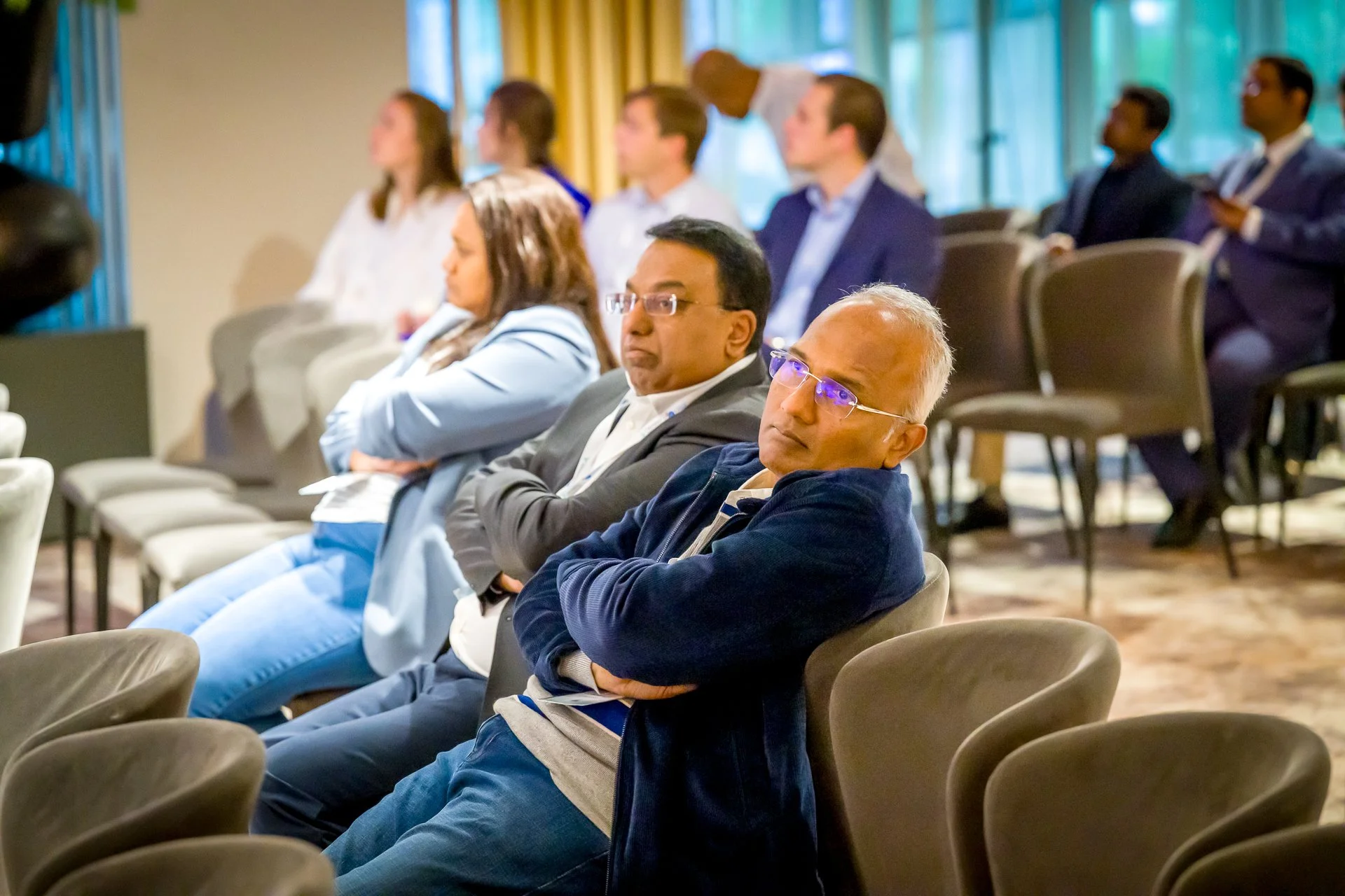 Des personnes assises lors d'une conférence, regardant vers l'avant, avec des expressions concentrées.