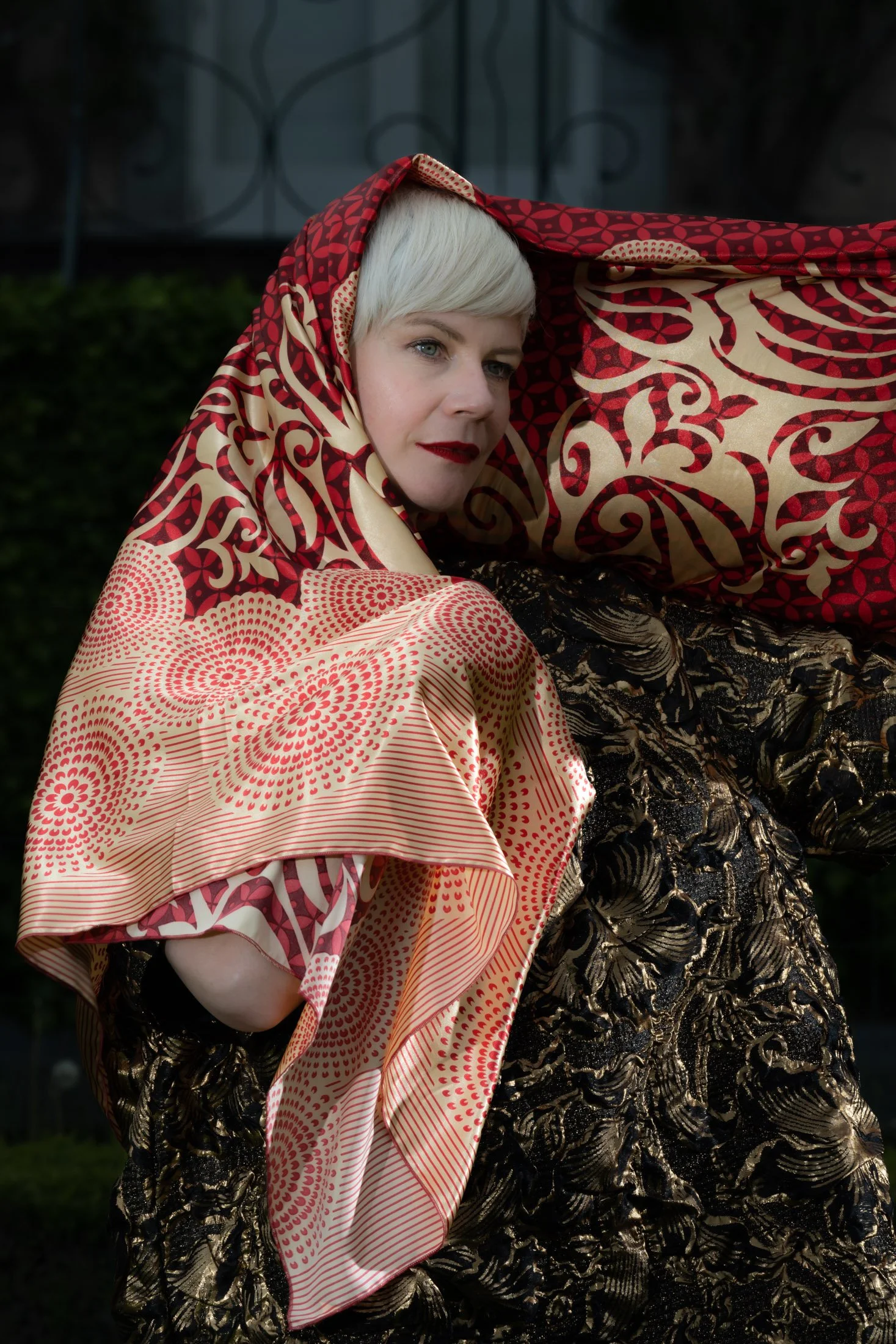 Femme avec un foulard rouge et doré, vêtue d'une robe noire ornée de motifs dorés.