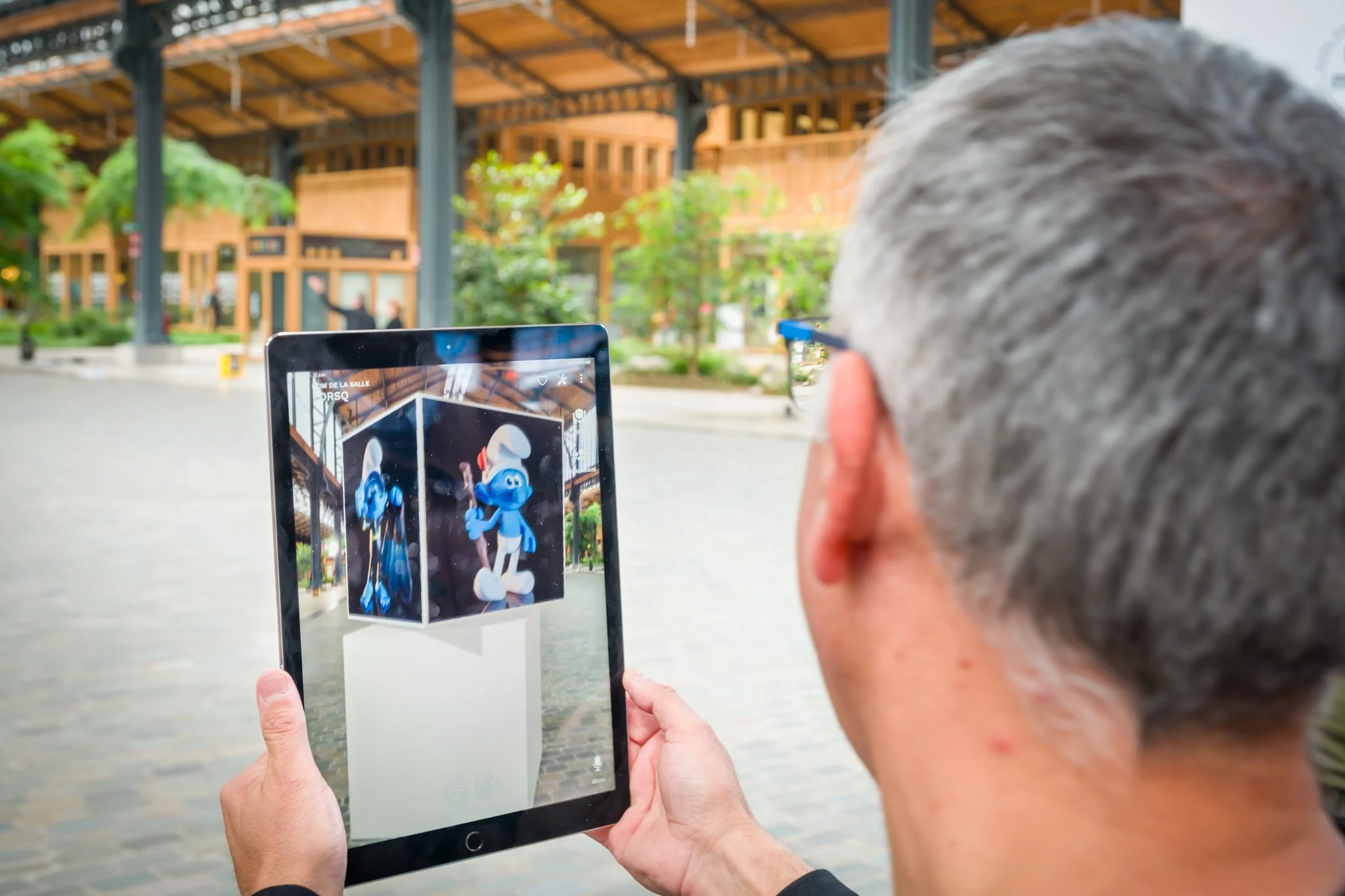 A person is holding a tablet showing cartoon characters on the screen, with a building in the background.