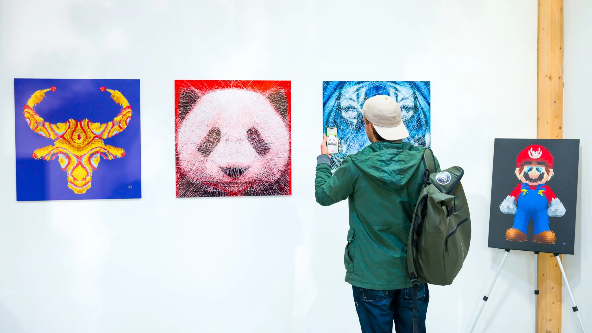 Un homme dans une galerie d'art regarde des œuvres modernes, dont un portrait numérique de panda et d'autres tableaux colorés